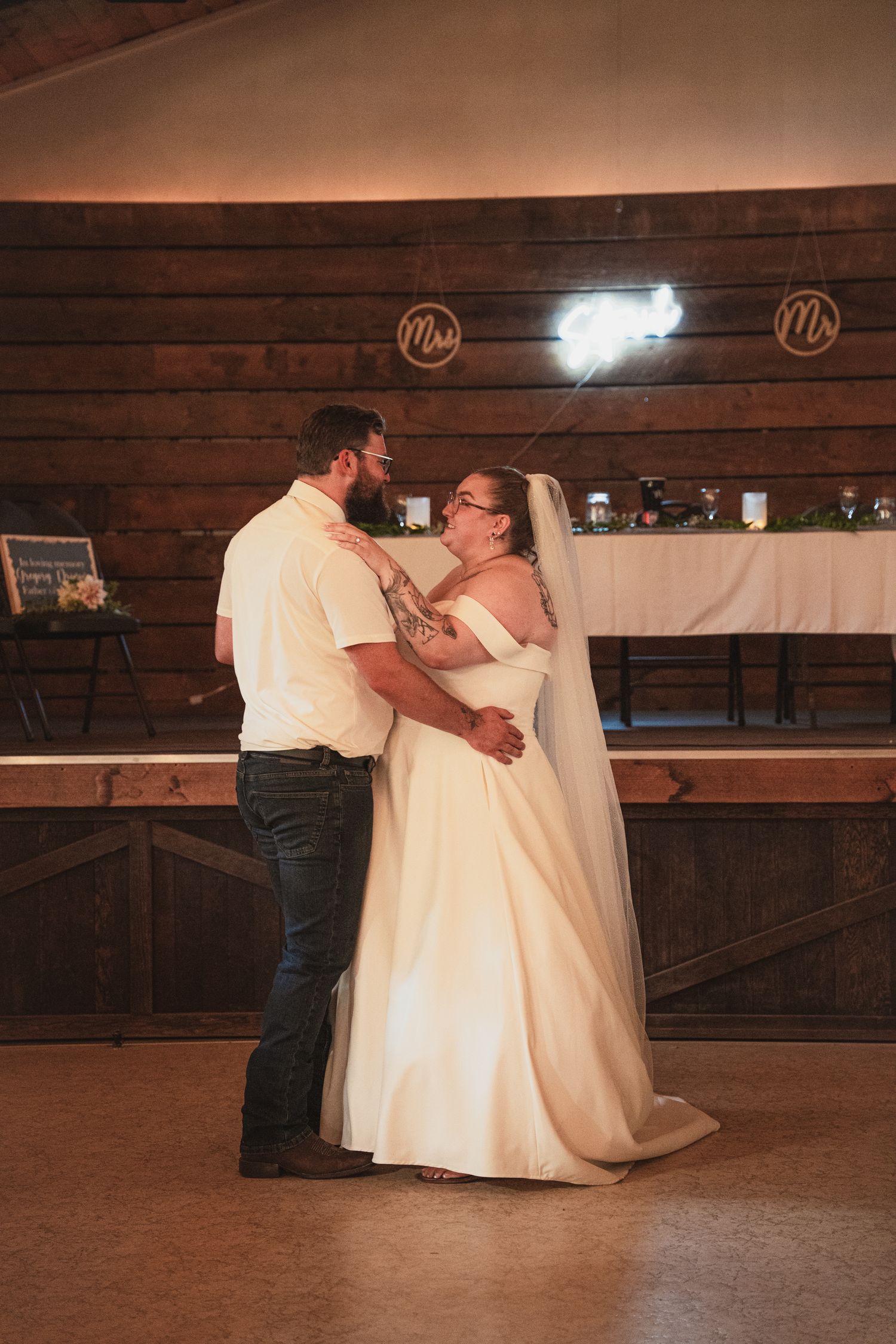 Bride and groom share their first dance in a rustic barn wedding venue with wooden walls and Mr. Mrs. signs.