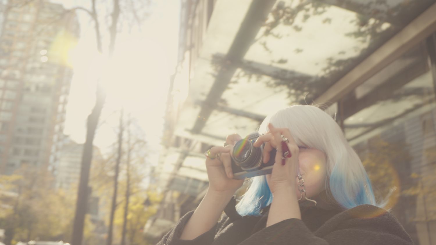 Woman with white hair using camera in sunlit urban setting.