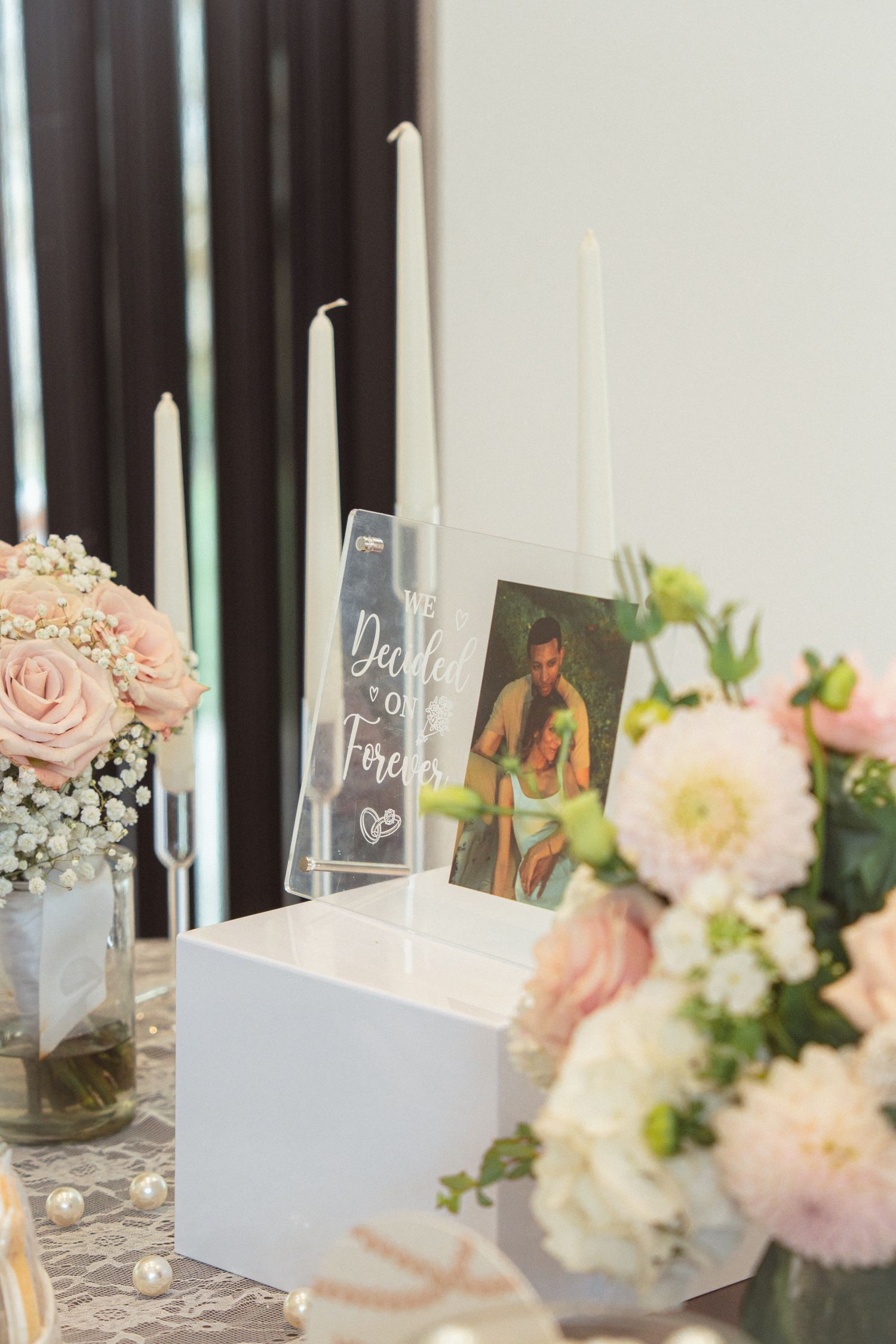 Elegant wedding unity candle setup with white tapered candles, a couples photo, and pink floral arrangements on a decorated table.