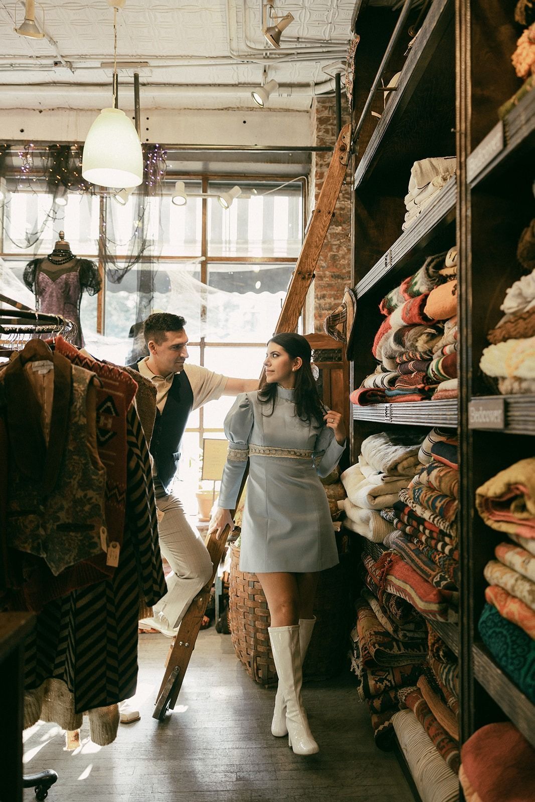 Couple browsing vintage clothing and textiles in a rustic boutique shop with wooden shelves.