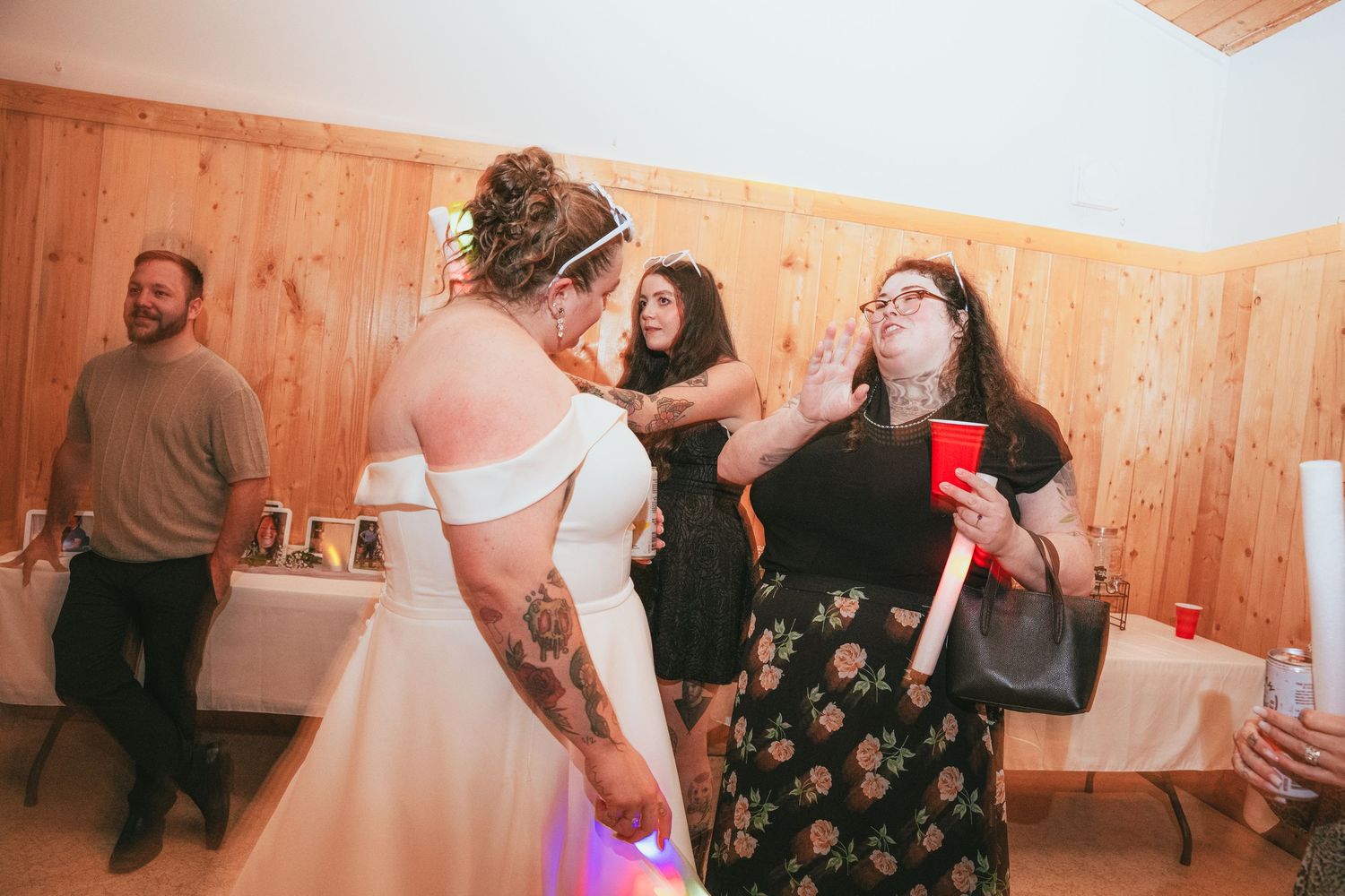 Bride in white gown with tattoos chatting with guest at rustic wedding reception.