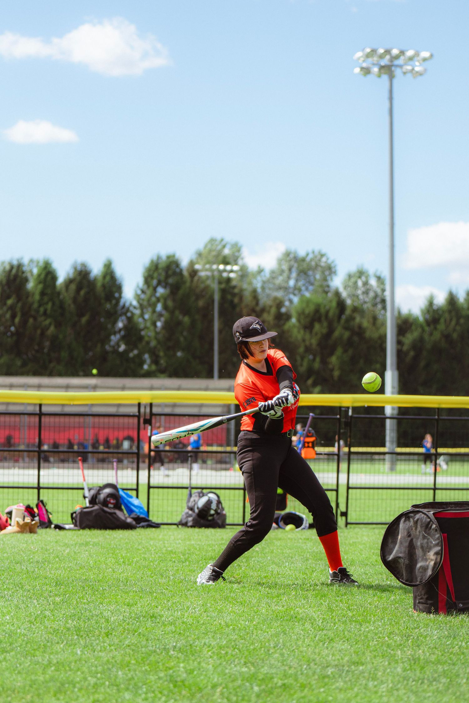 Female softball player hitting ball during sunny outdoor practice session.