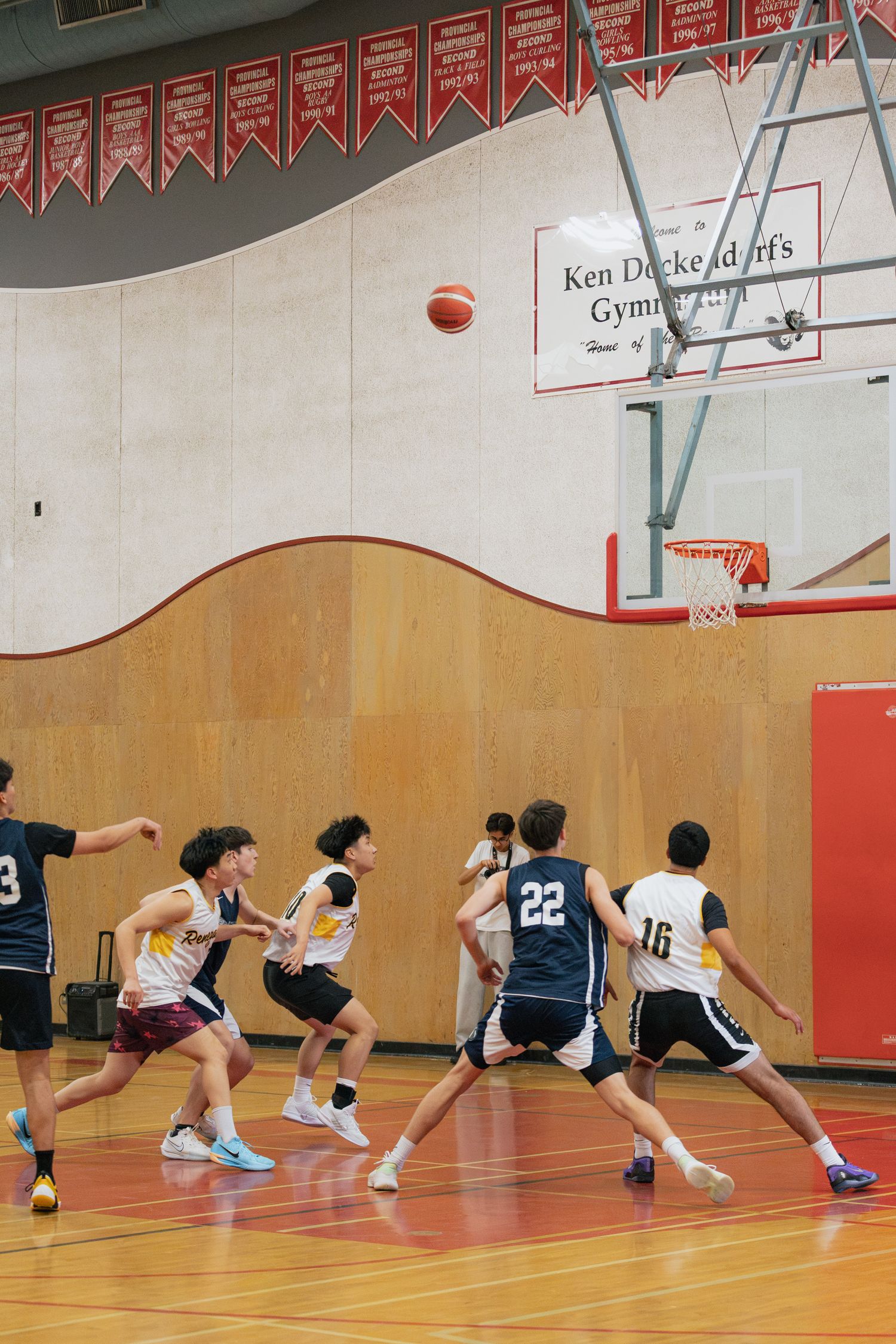 Youth basketball players compete in Ken Dockendorf Gymnasium with navy and white-uniformed teams during active play.
