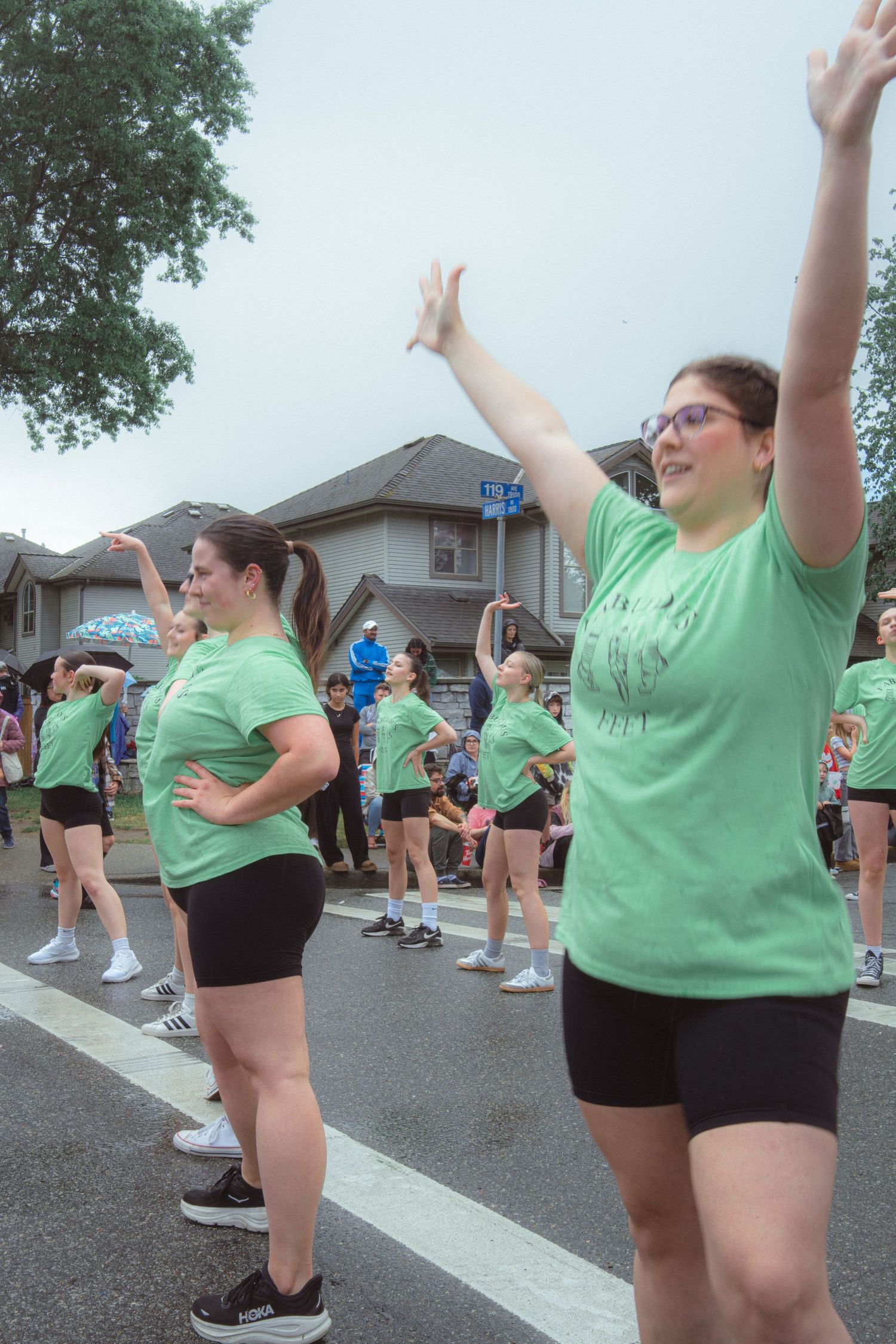 A group of women in matching green shirts perform a dance routine in a street parade.