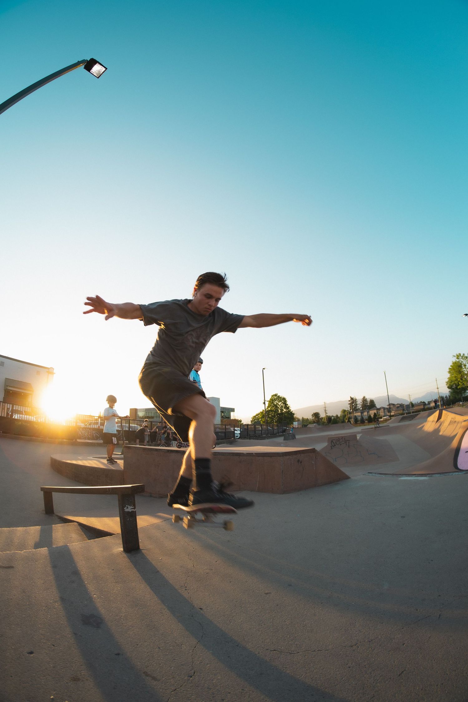 Skateboarder balancing on a rail with arms outstretched at a skate park during sunset.