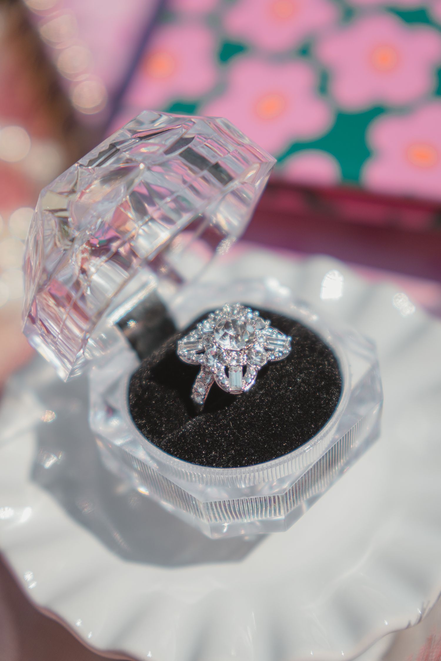 Elegant diamond halo engagement ring displayed in a crystal ring box on a white ceramic dish.