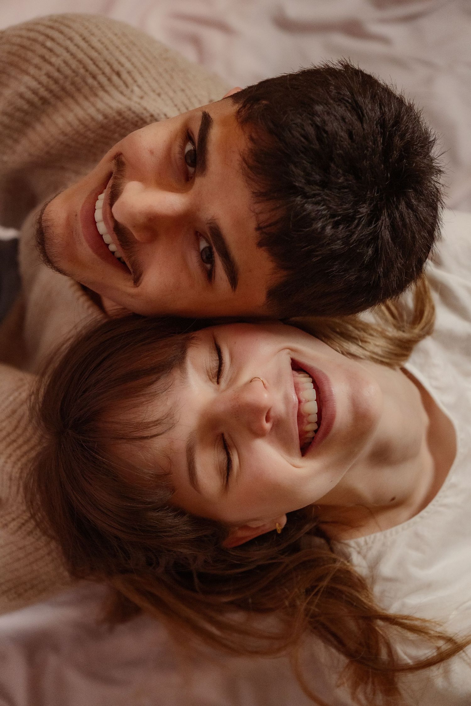 Overhead view of laughing young couple lying head to head on a white surface.