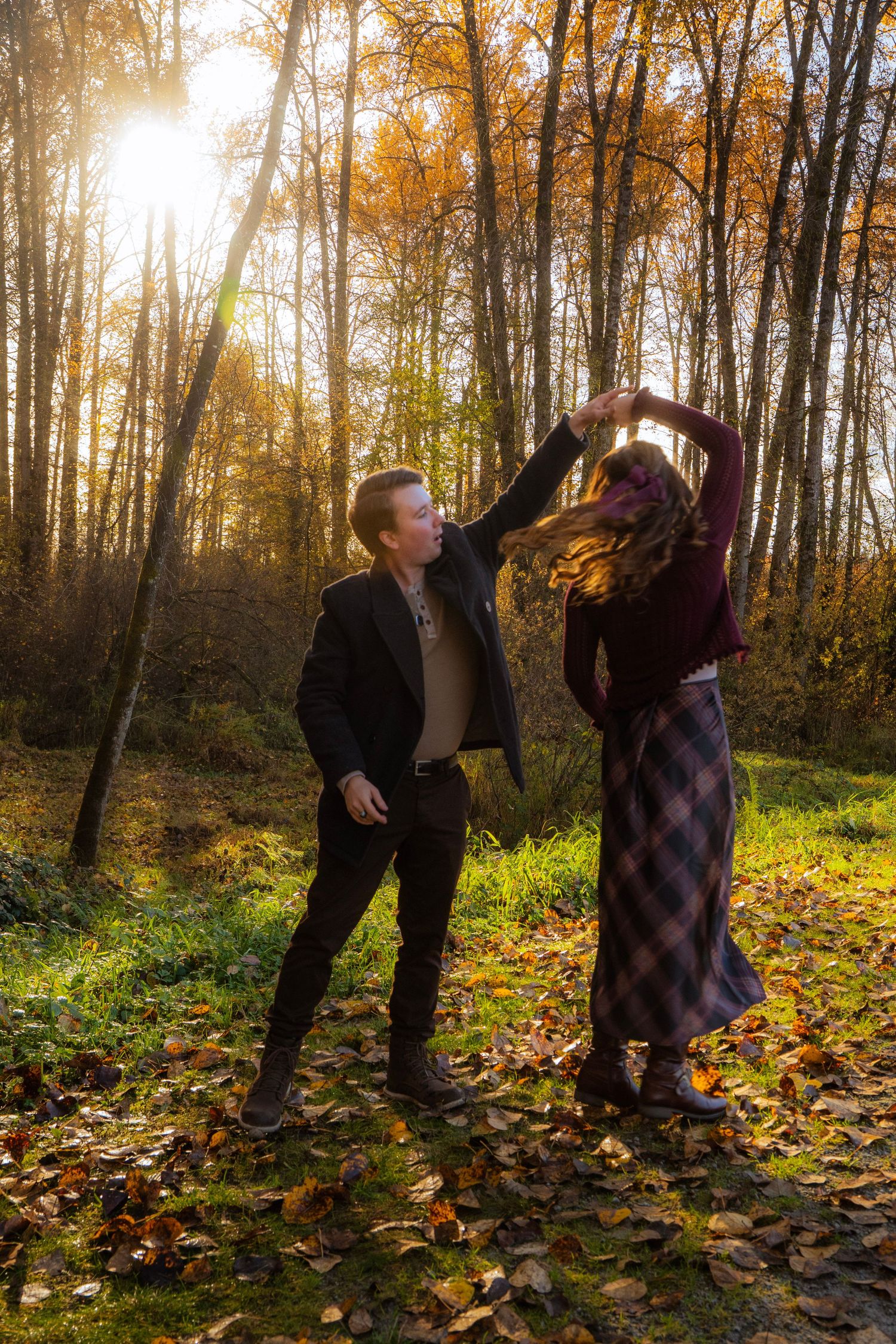 Couple dancing together in a radiant autumn forest with golden sunlight and colorful fallen leaves around them.
