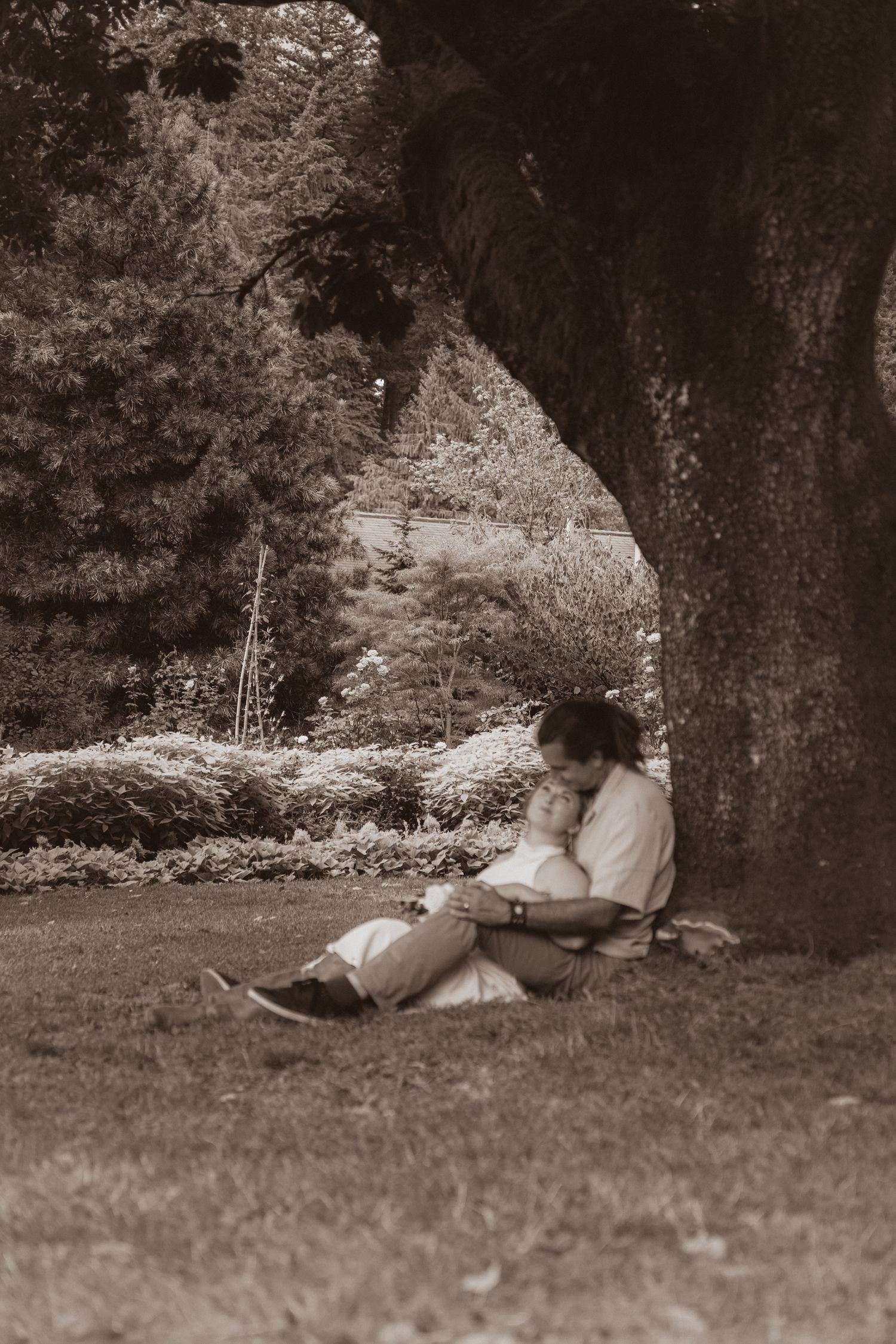 Sepia-toned photo of a couple sitting together under a large tree in a peaceful park.