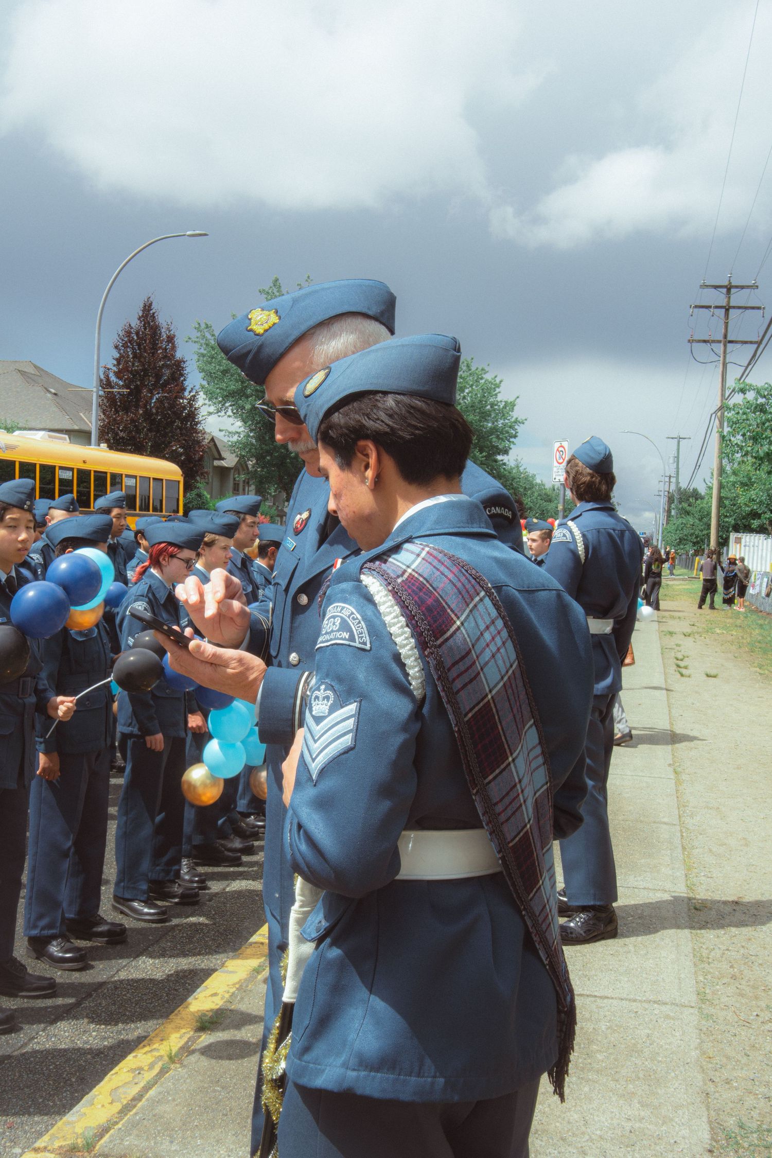 Air cadets in blue uniforms holding colorful balloons line up along a street during a parade.