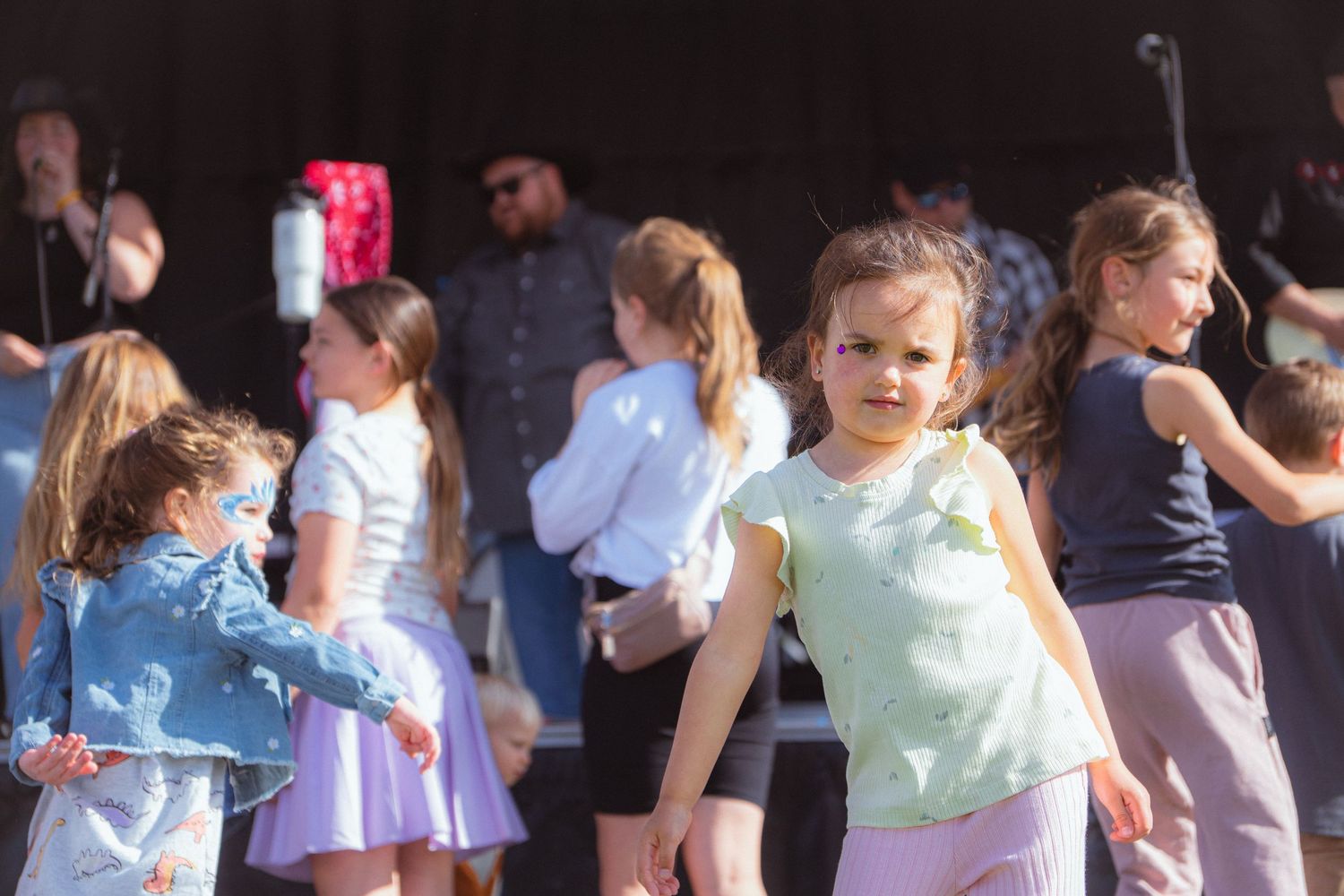 Young girls dancing outdoors at a live music festival on a sunny day.