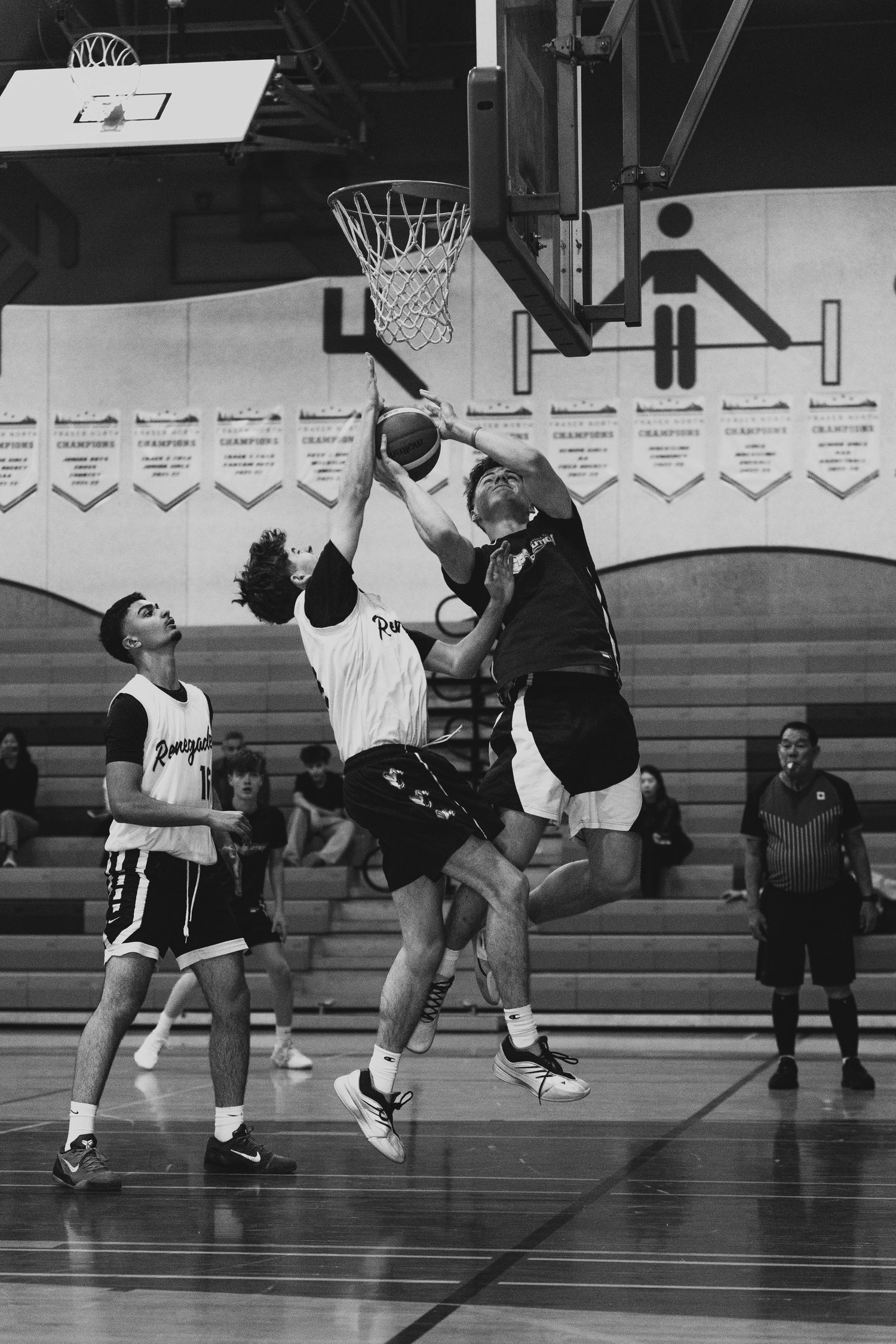 Players compete for a rebound under the basketball hoop during an intense indoor game.