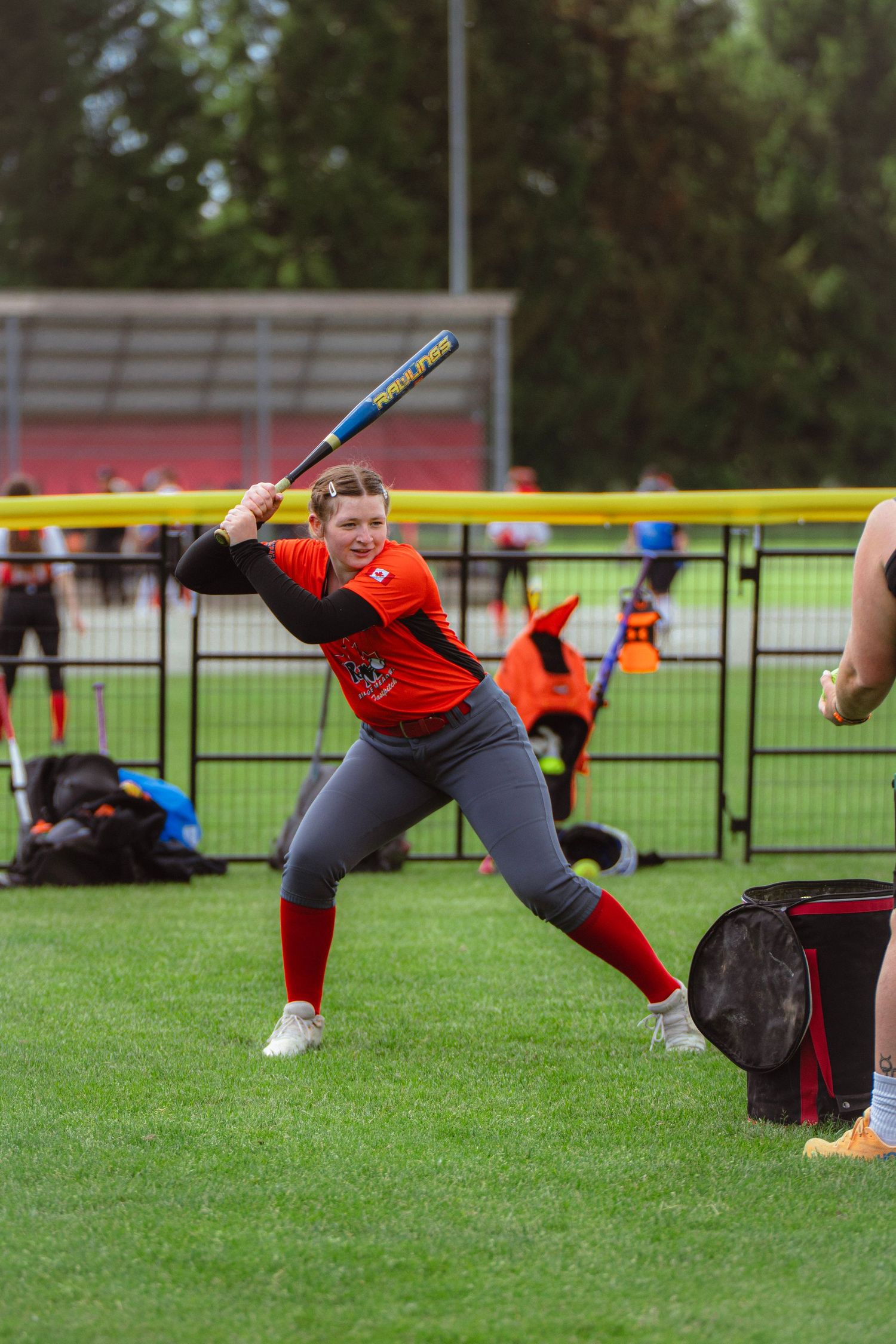 Female softball player in red and black uniform in batting stance on green field.