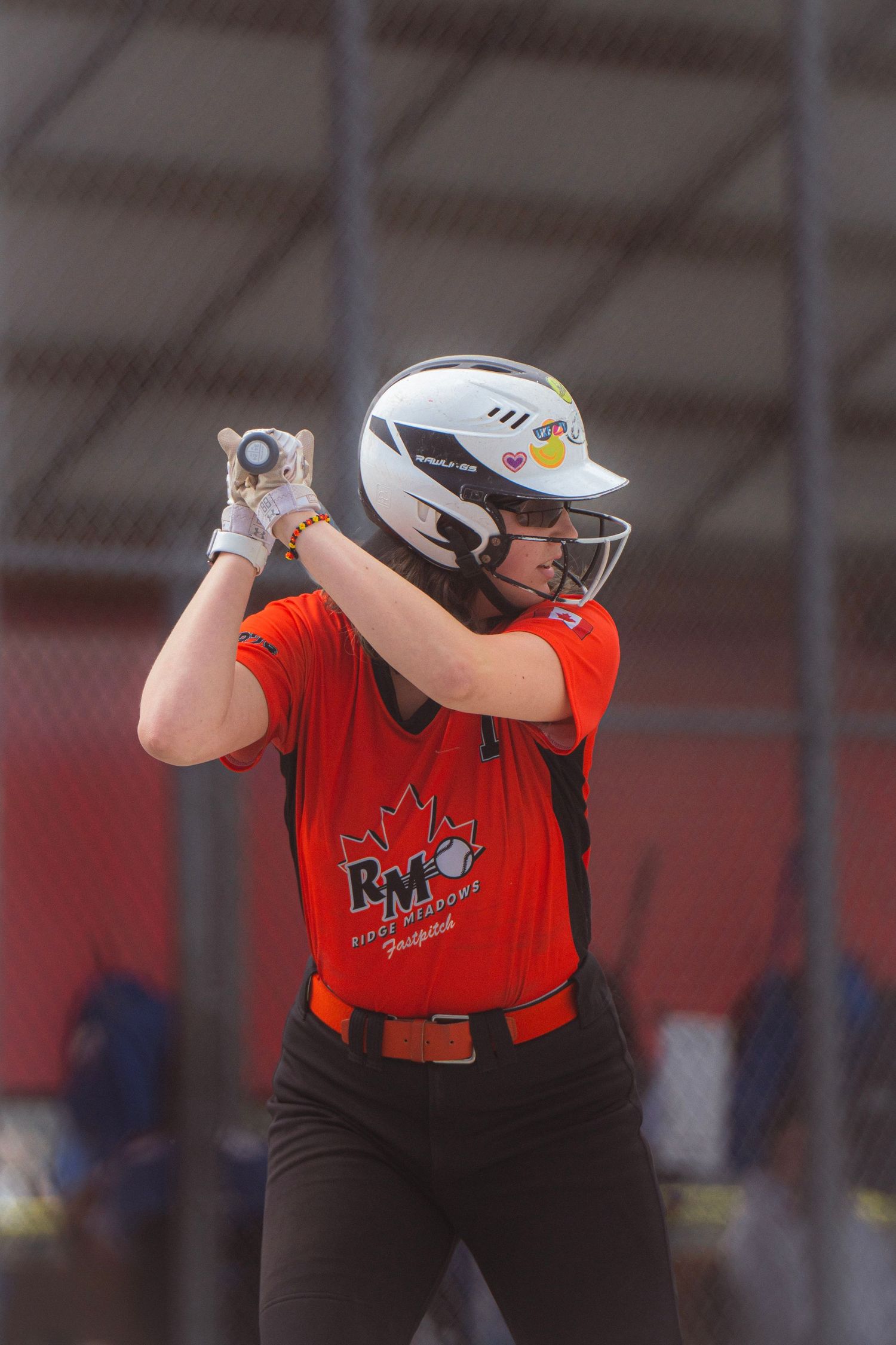 Close-up of softball batter in orange RMO uniform in batting stance wearing a white helmet.