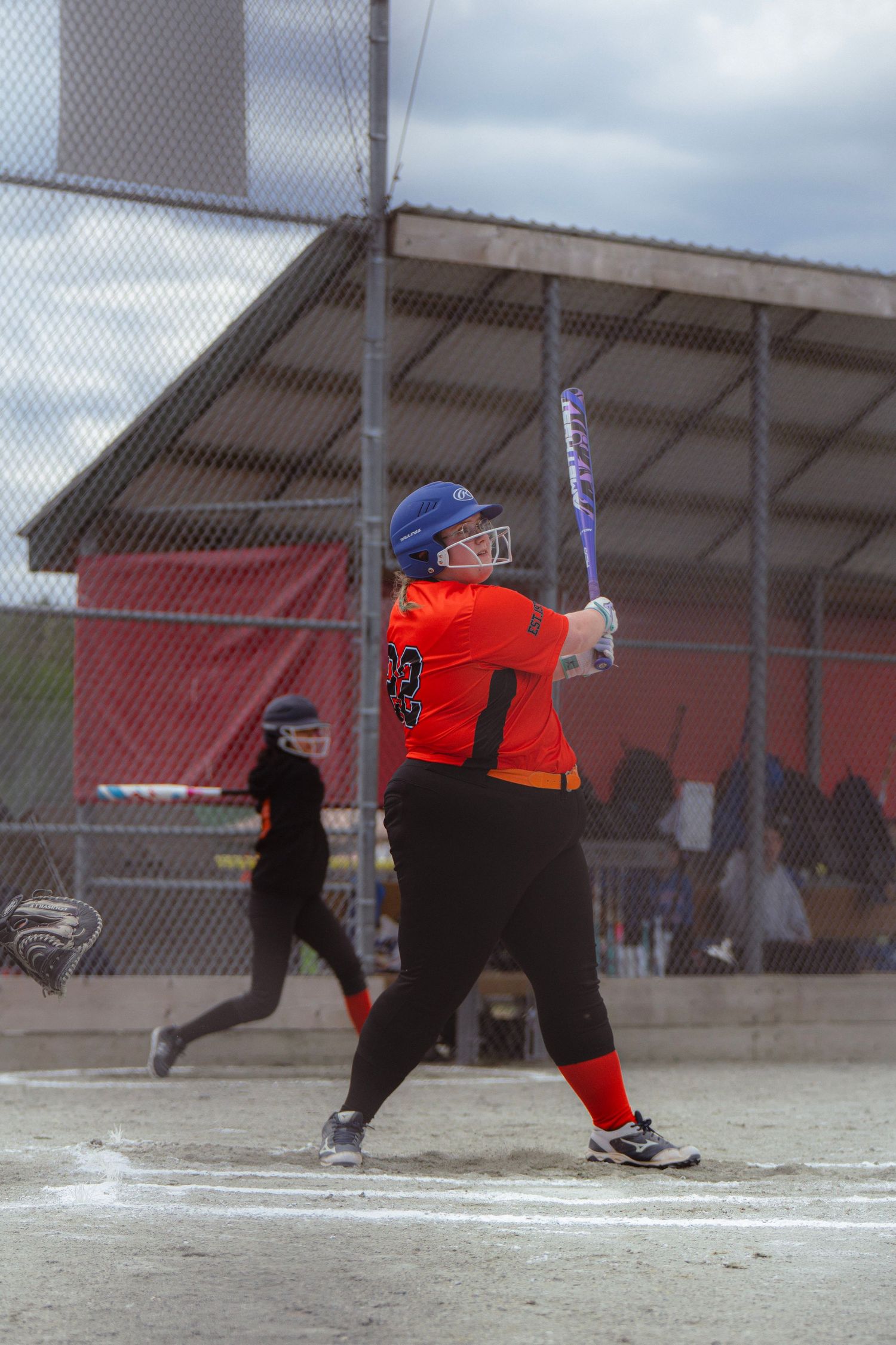 Female softball player in orange jersey with number 23 batting at home plate.