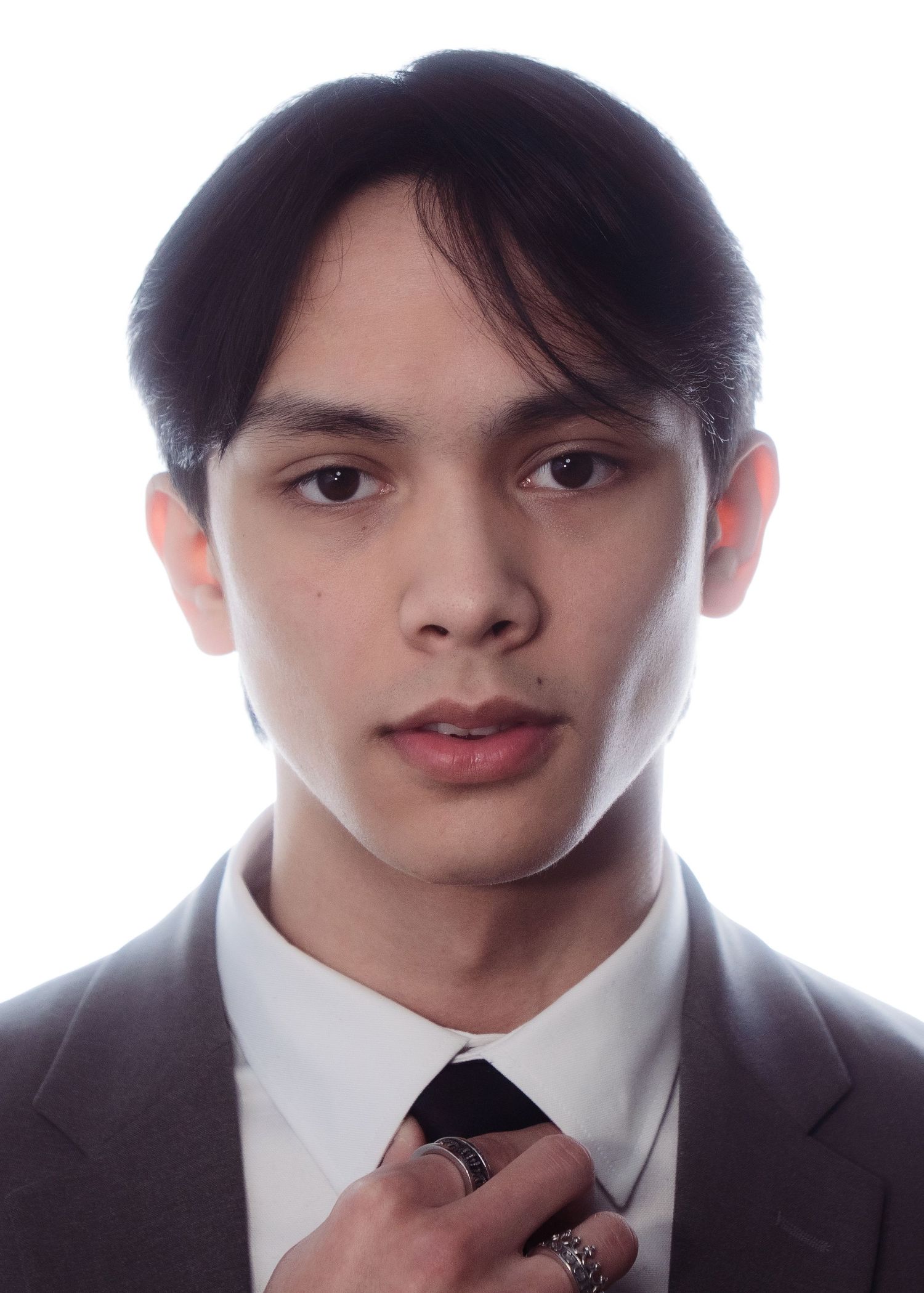 Young man with dark hair adjusting his tie, wearing a suit, close-up professional portrait on white background.