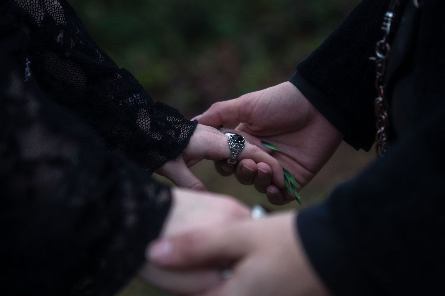 Close-up of hands exchanging a ring during a gothic-style wedding ceremony outdoors.