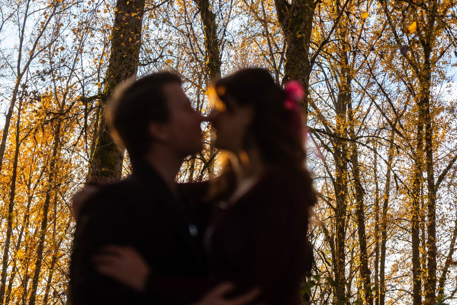 Romantic couple about to kiss in soft focus with golden autumn trees in background.