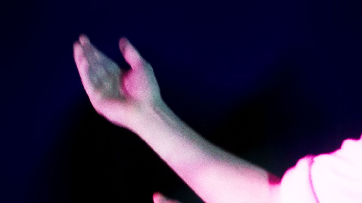A single arm raised against a dark background illuminated by soft pink stage lighting.