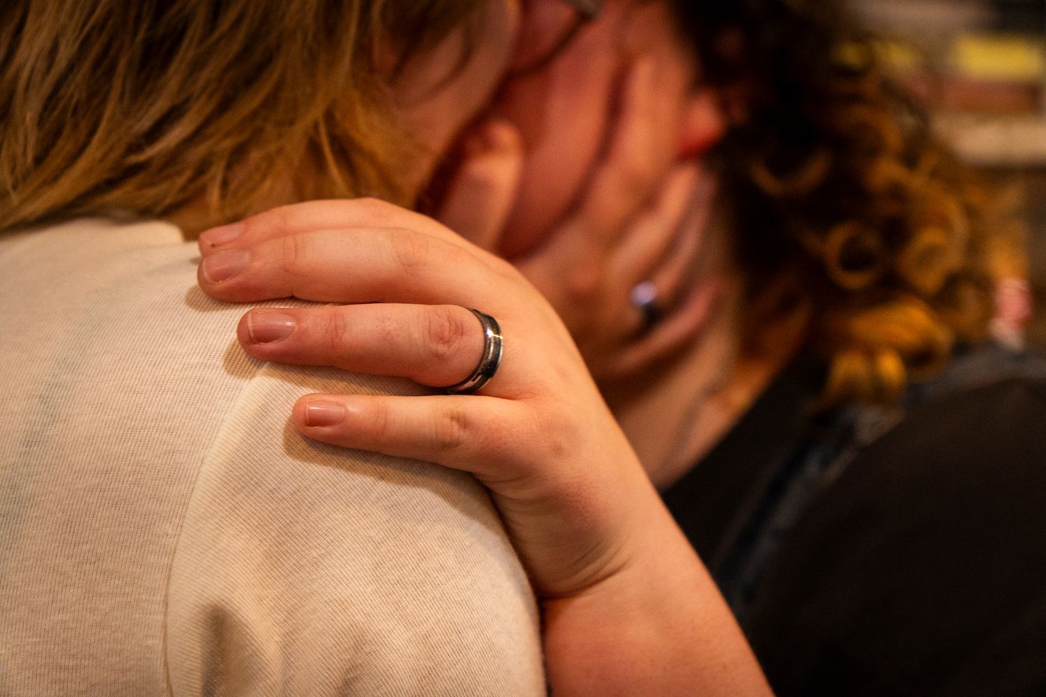 A person with a black ring on their finger gently placing their hand on someone's shoulder in an embrace.