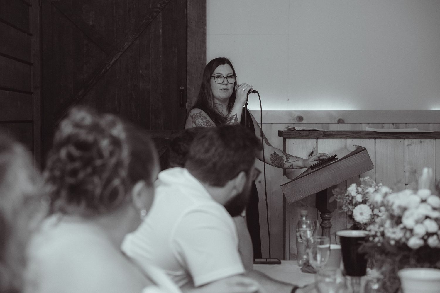 Woman speaks at podium microphone during wedding reception speech in black and white photo.