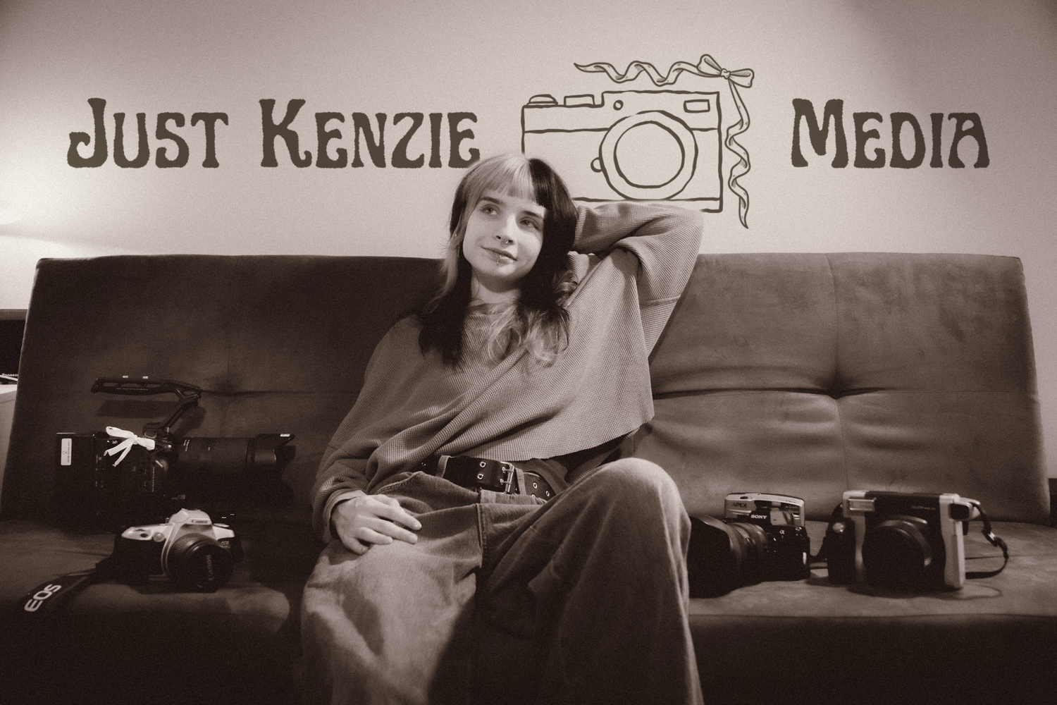Young woman poses on a couch surrounded by vintage cameras under Just Kenzie Media logo sign.
