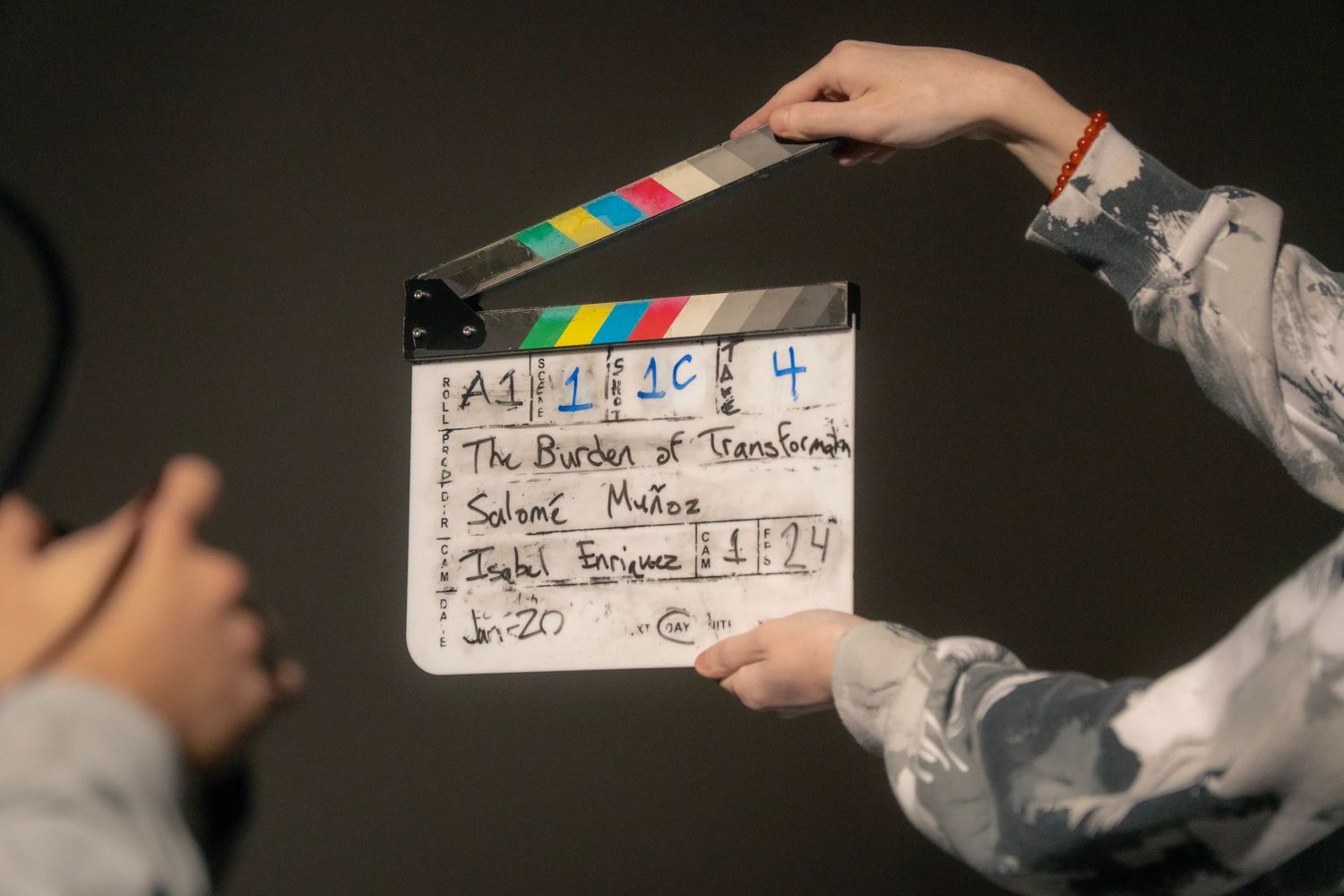 A film clapperboard held up on a movie set, displaying scene details for The Burden of Transformation.