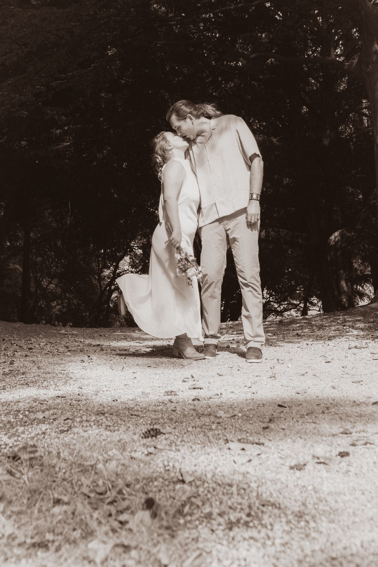 Romantic sepia-toned photo of a couple sharing a kiss on a woodland path.