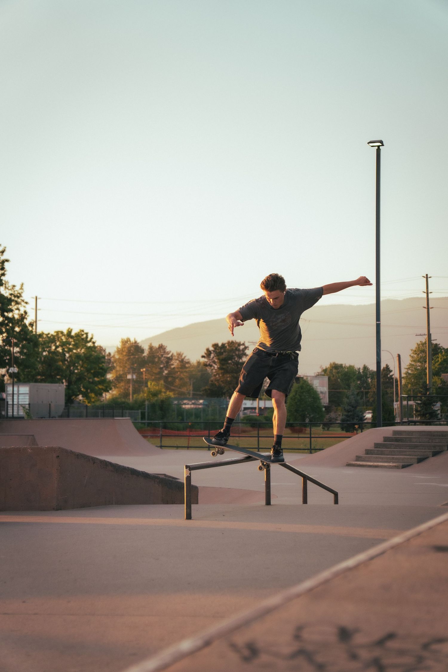 Skateboarder grinding a metal rail at an outdoor skate park during golden hour sunset.