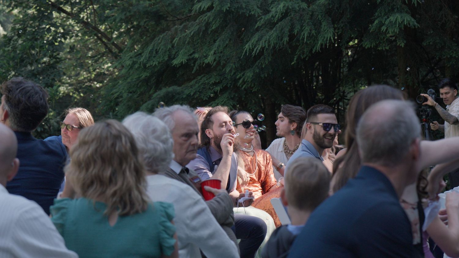 Wedding guests seated outdoors smile and celebrate during an elegant garden wedding ceremony.