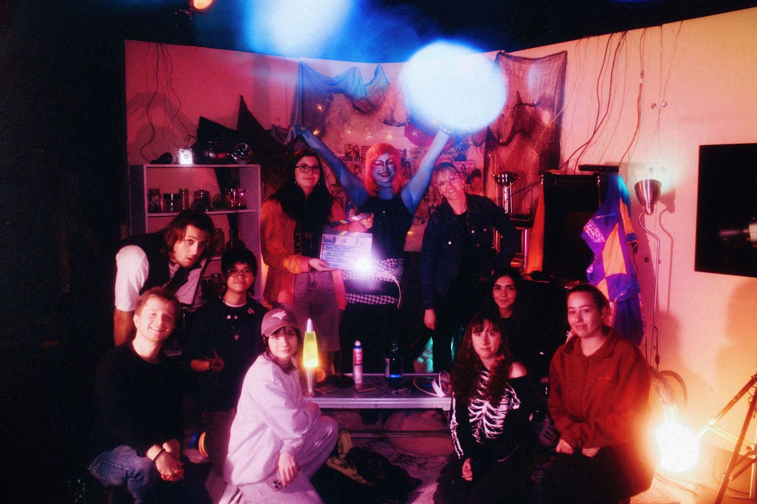 Group of people posing together under colorful blue and pink lights in a dark room.