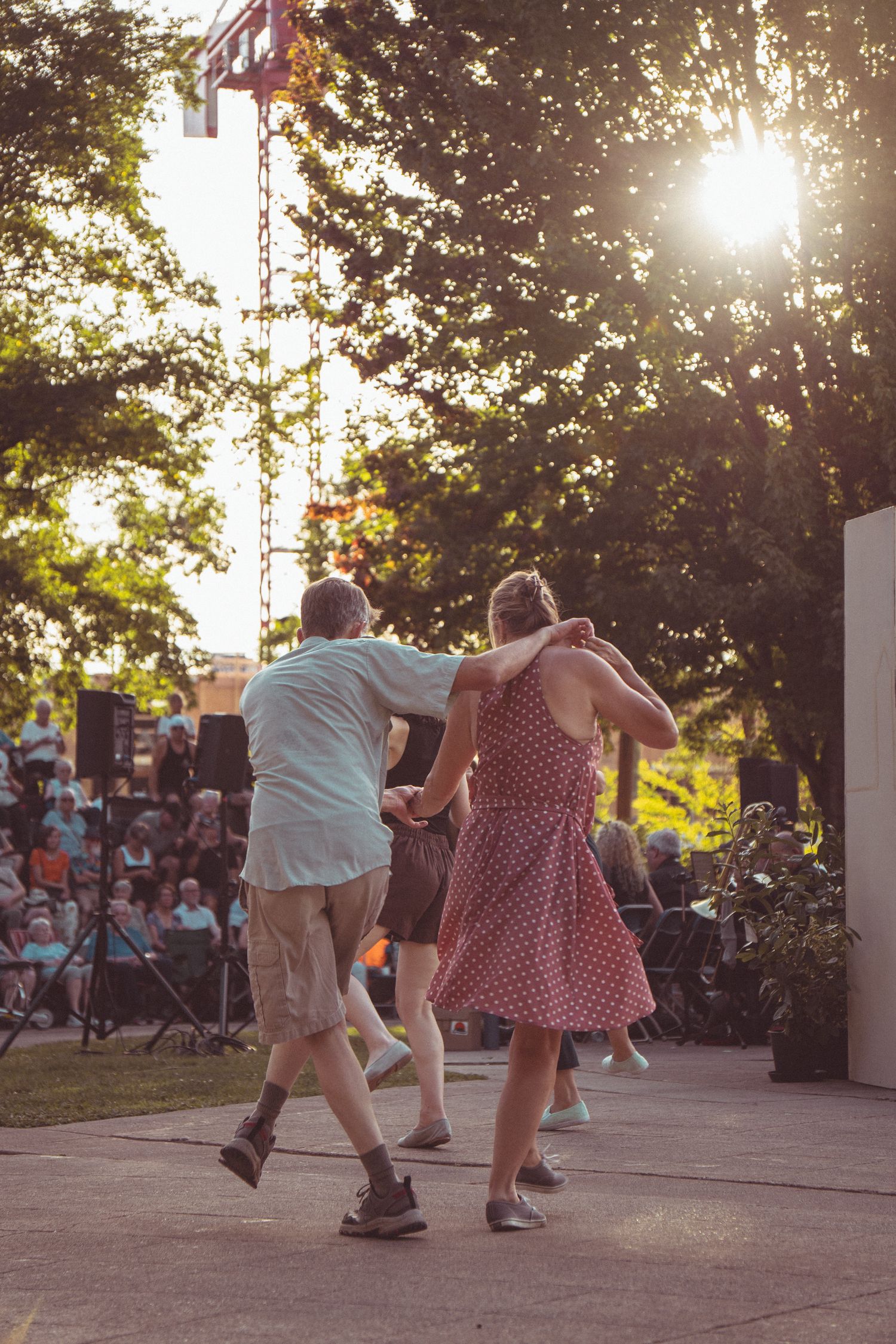 Couple dancing together on an outdoor stage at sunset during a live music event in a park.