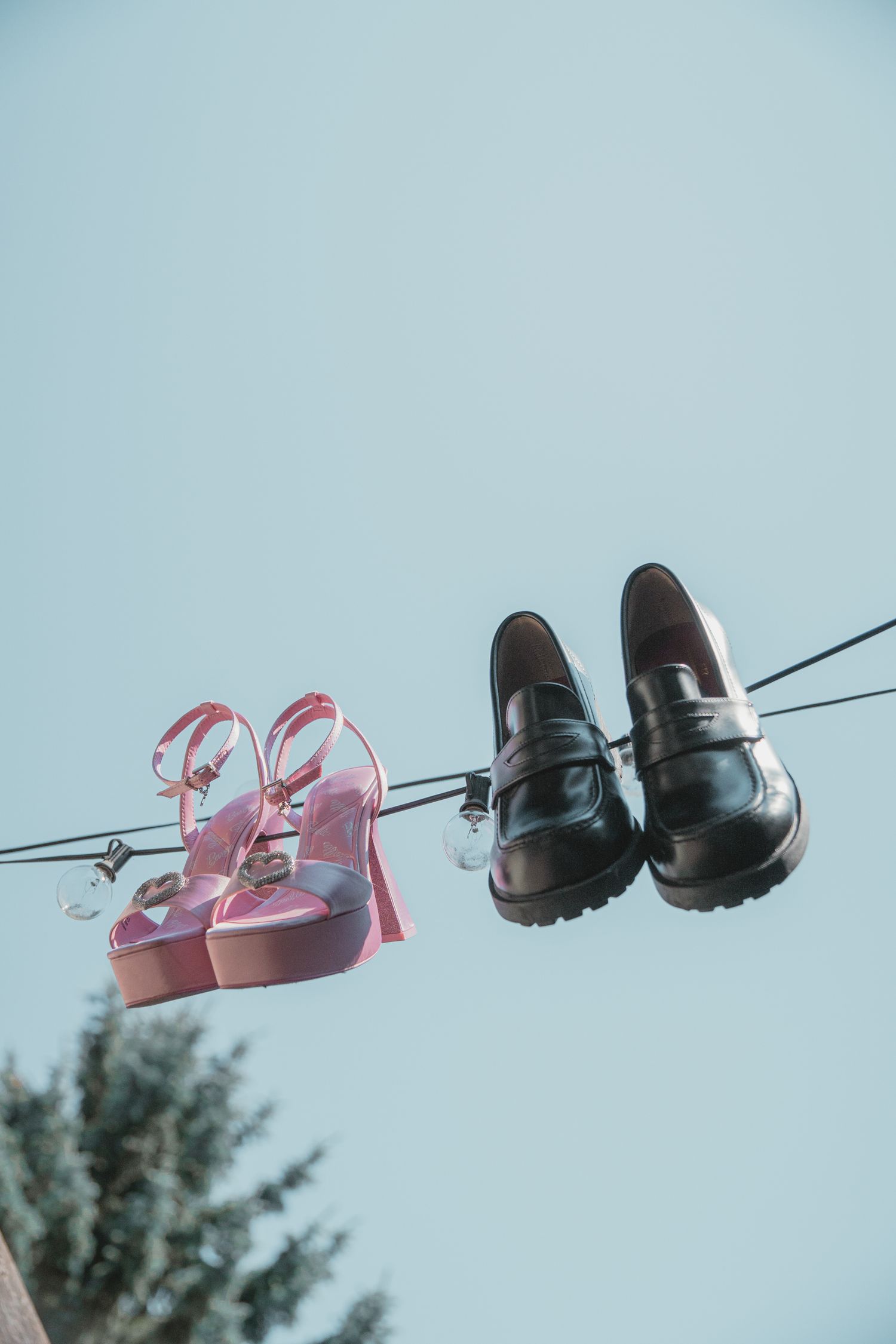 Pink high heels and black loafers hanging on a wire against a clear blue sky.