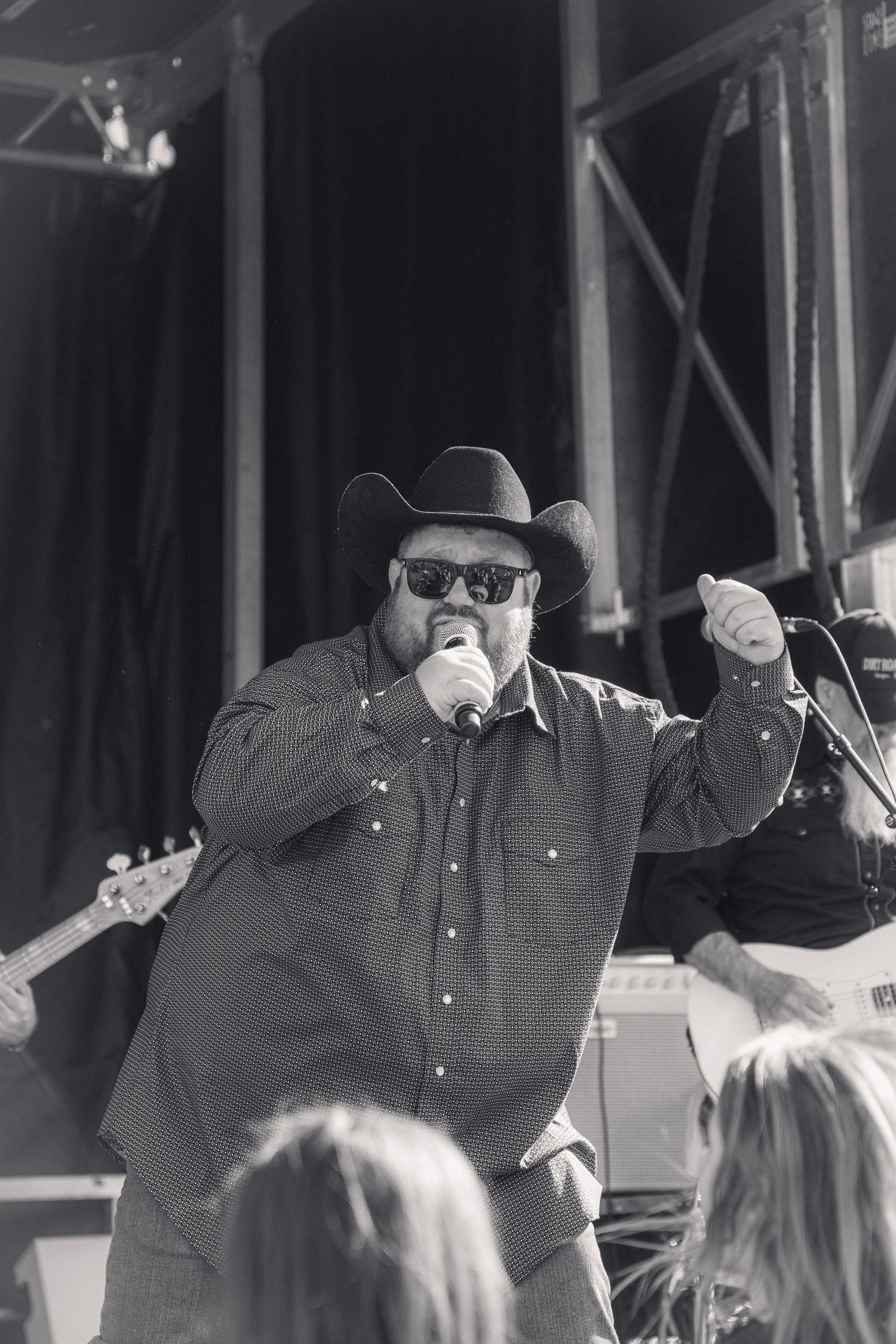 Country singer in cowboy hat performing on stage with microphone at outdoor festival.