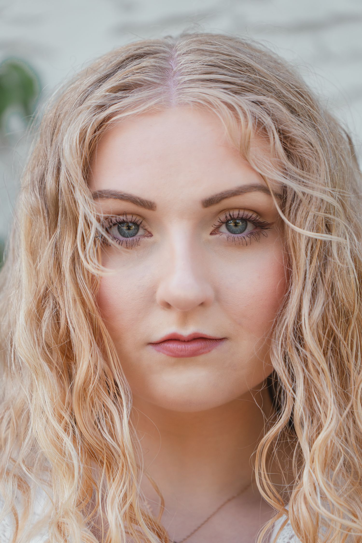 Close-up portrait of a young woman with curly blonde hair and green eyes wearing natural makeup.