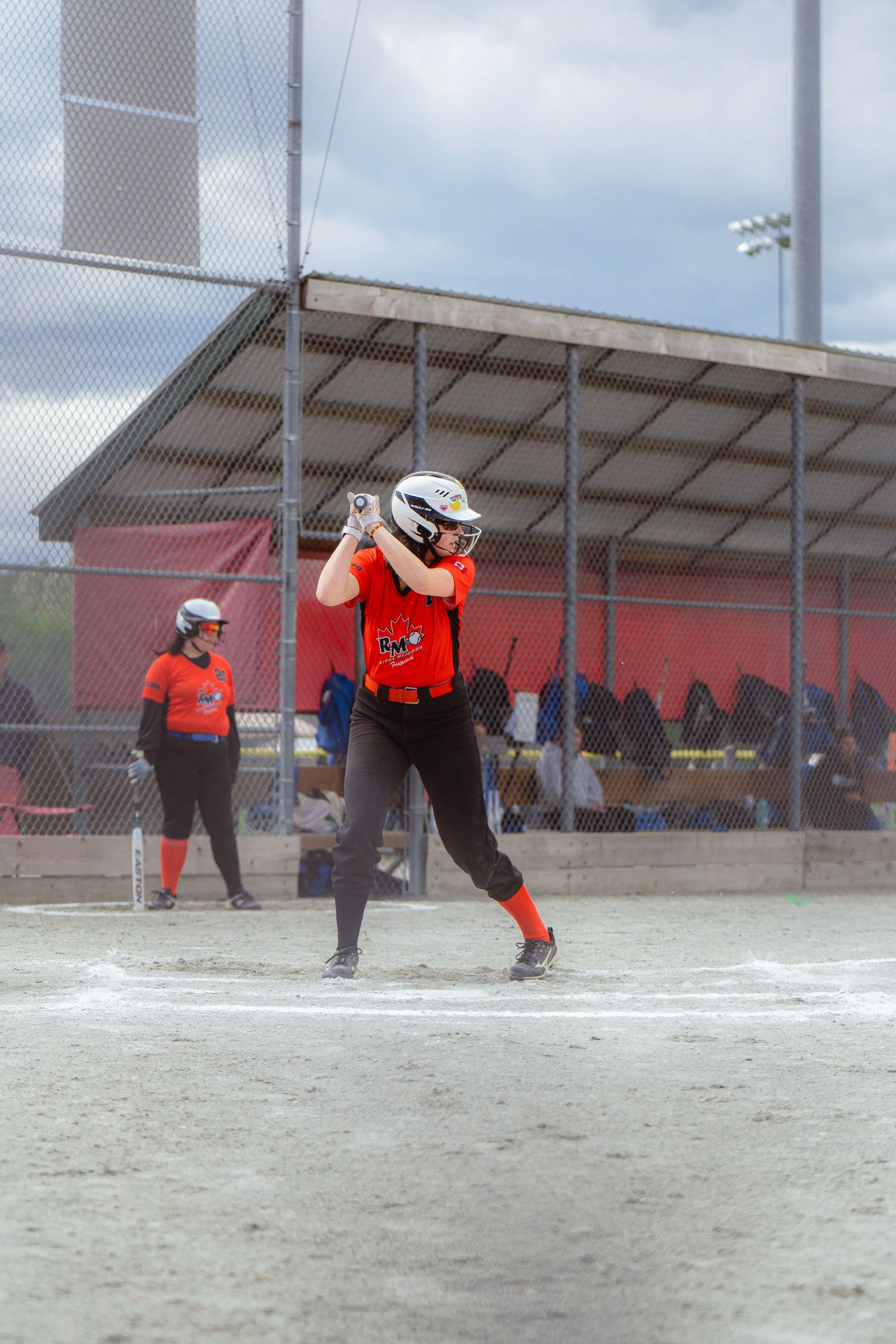 Female softball player in orange uniform takes a powerful swing at the plate during a game.