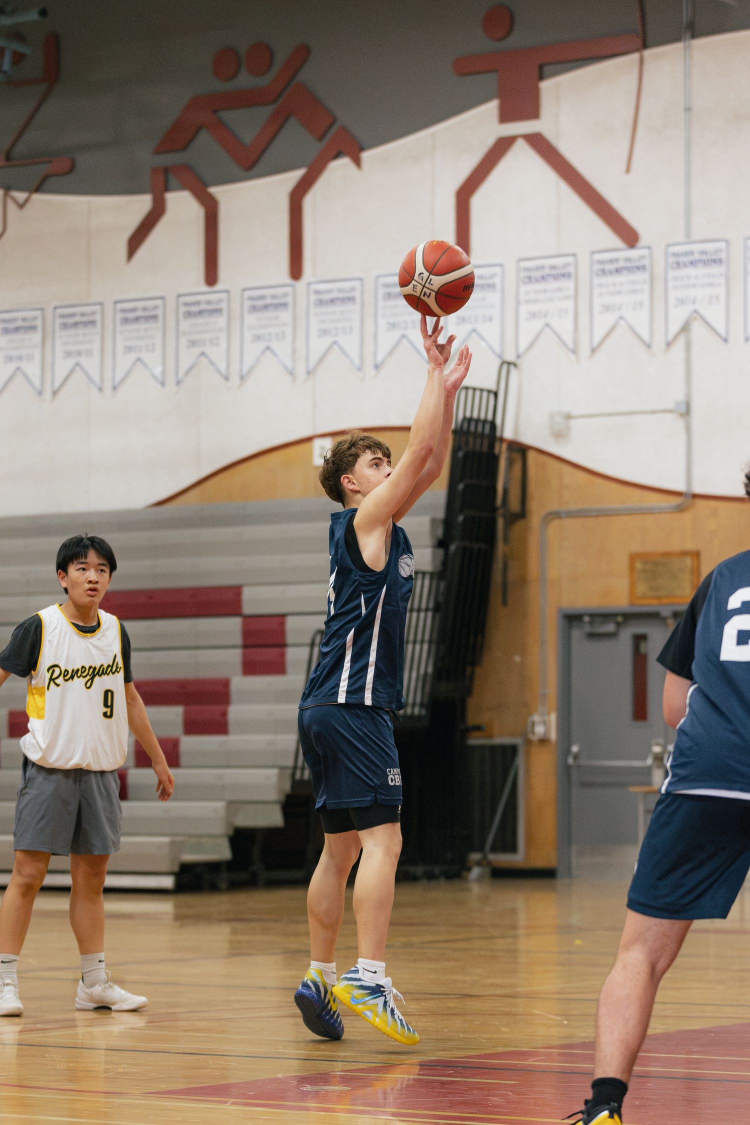 Young basketball player in navy uniform shoots a jump shot during an indoor gymnasium game.
