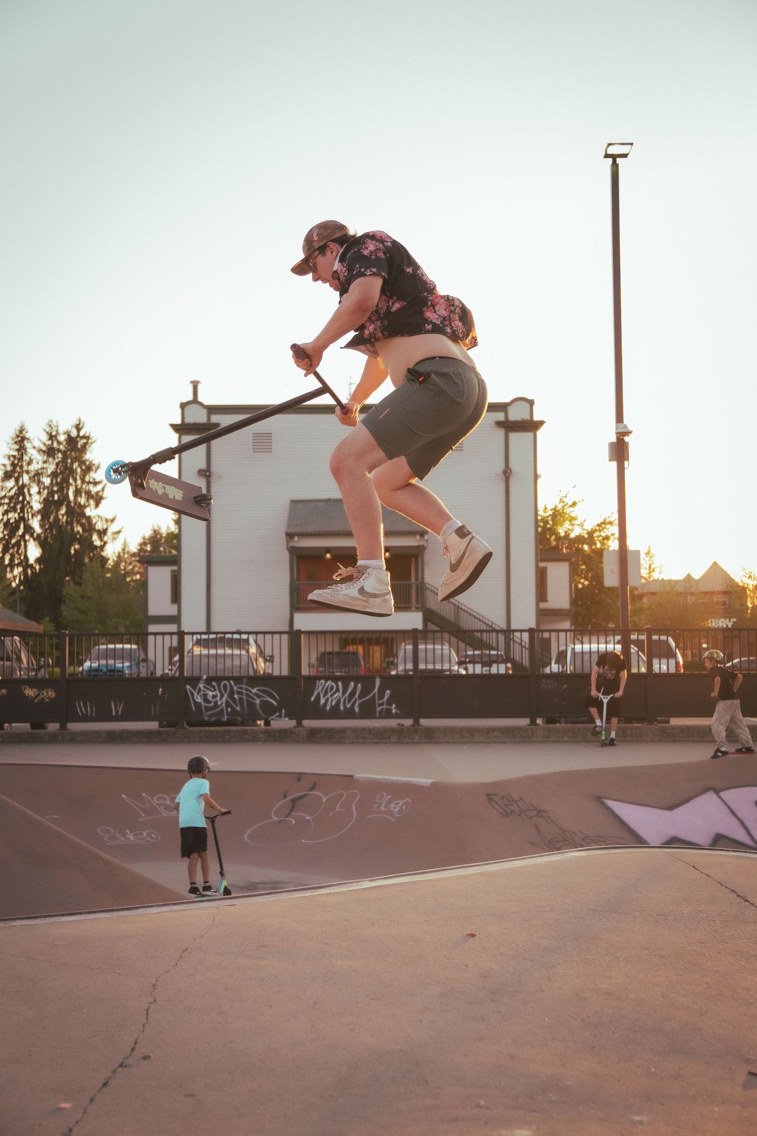 Young man doing aerial trick on a stunt scooter at a skate park during golden hour.