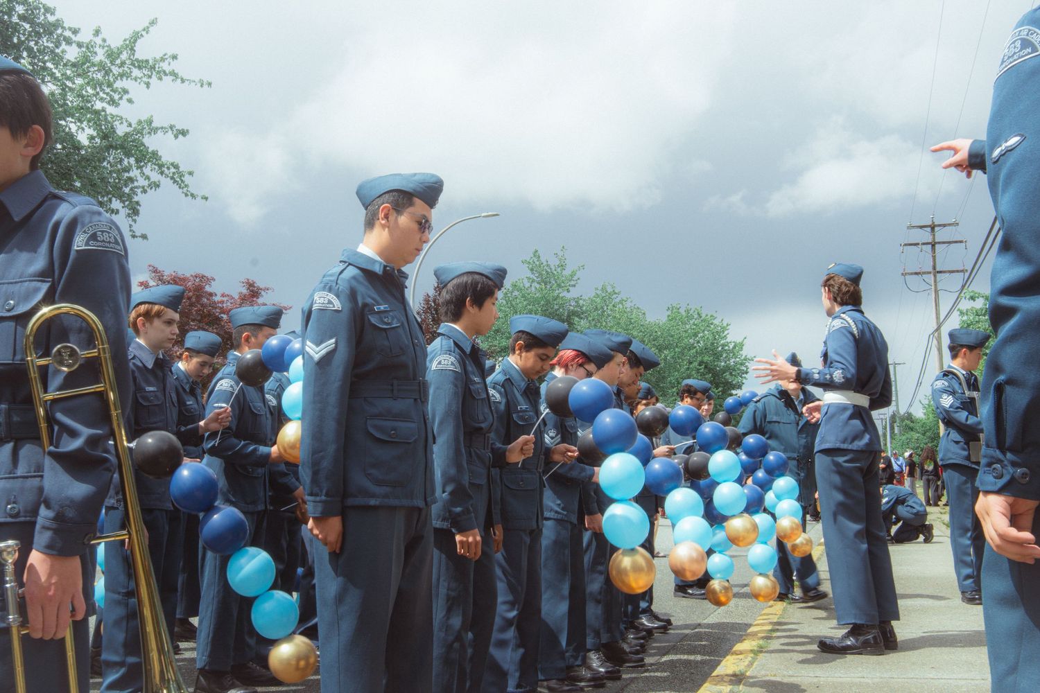Air cadets in blue uniforms stand in formation holding blue and gold balloons before a parade.