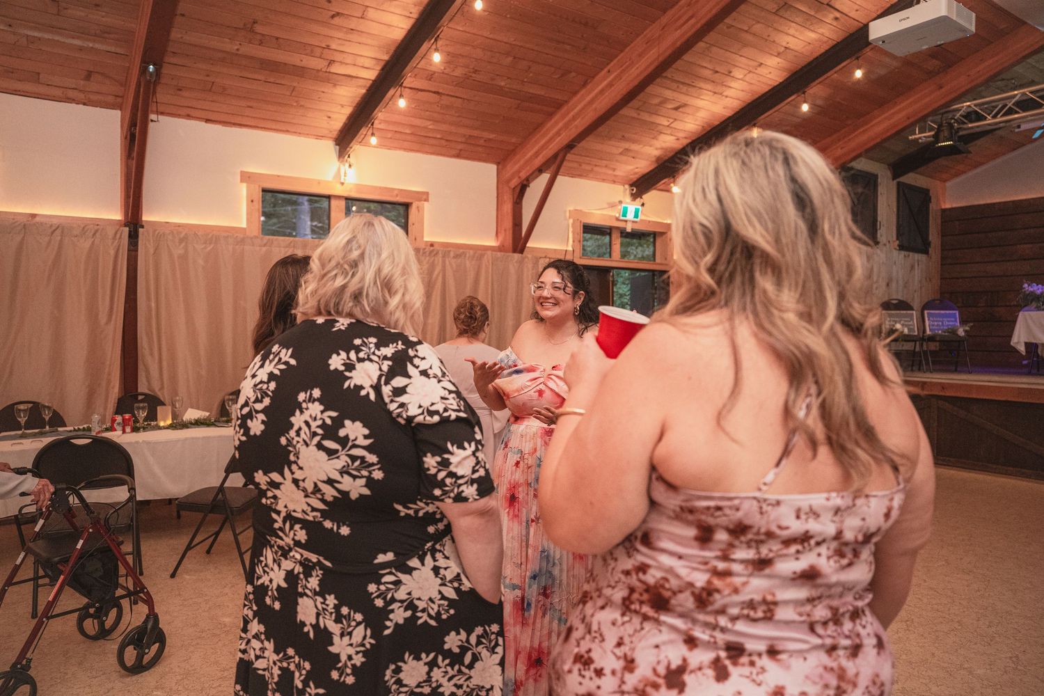 Wedding guests in floral dresses mingling and chatting on the dance floor at a rustic reception venue.