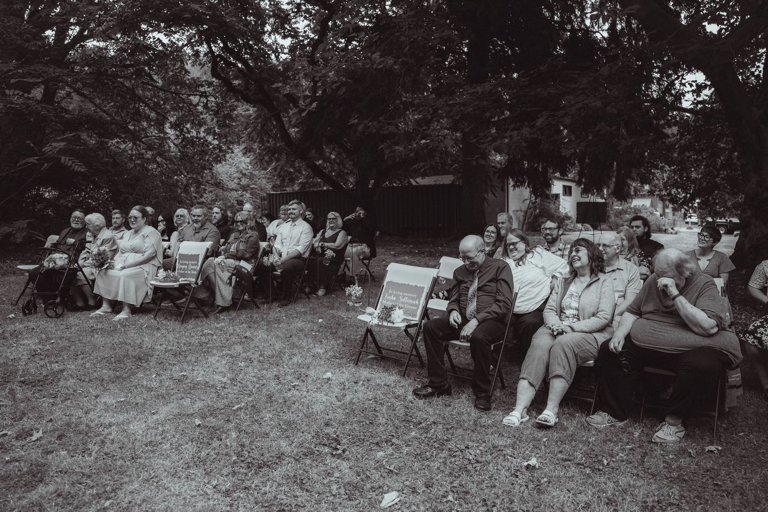 Black and white photo of a large group of people seated outdoors on chairs in a garden setting.