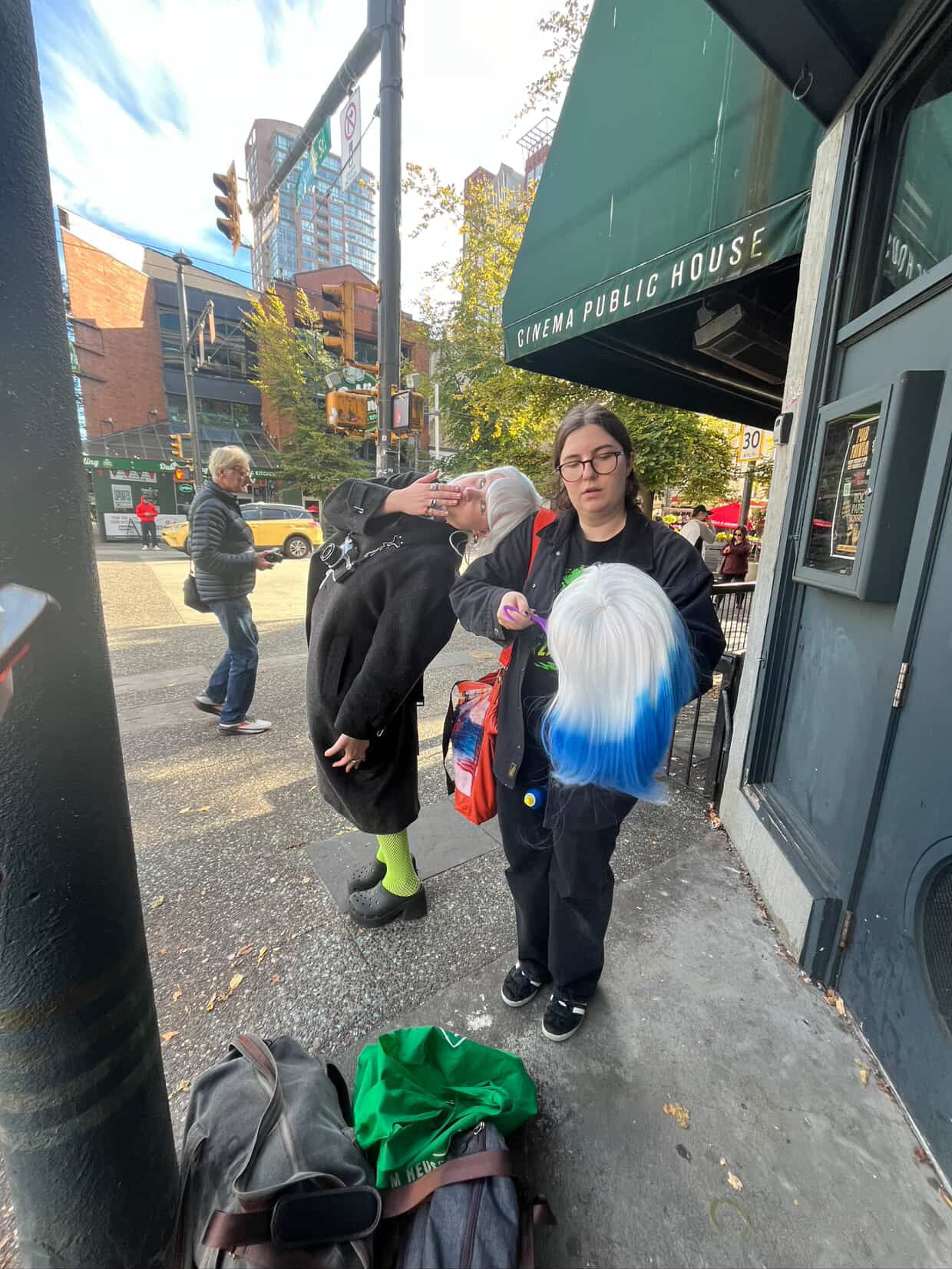People standing outside Cinema Public House wearing colorful wigs on a city sidewalk.