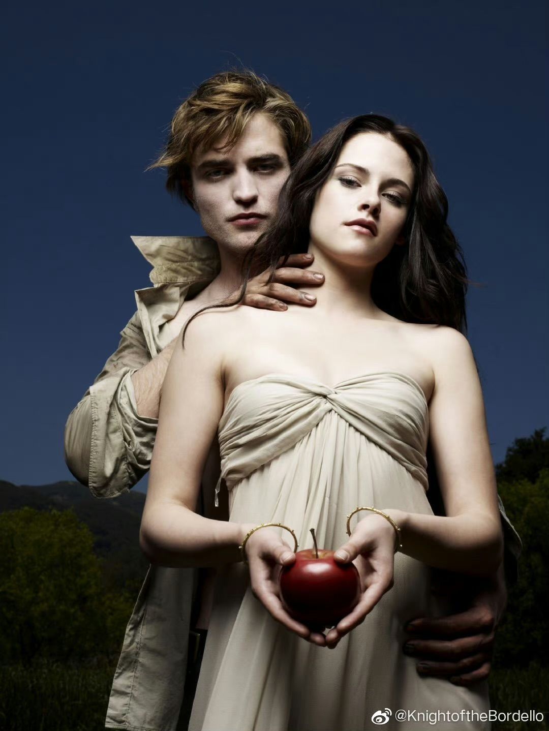 Young couple in romantic pose, woman holding red heart-shaped apple, styled in soft earth tones against blue sky.
