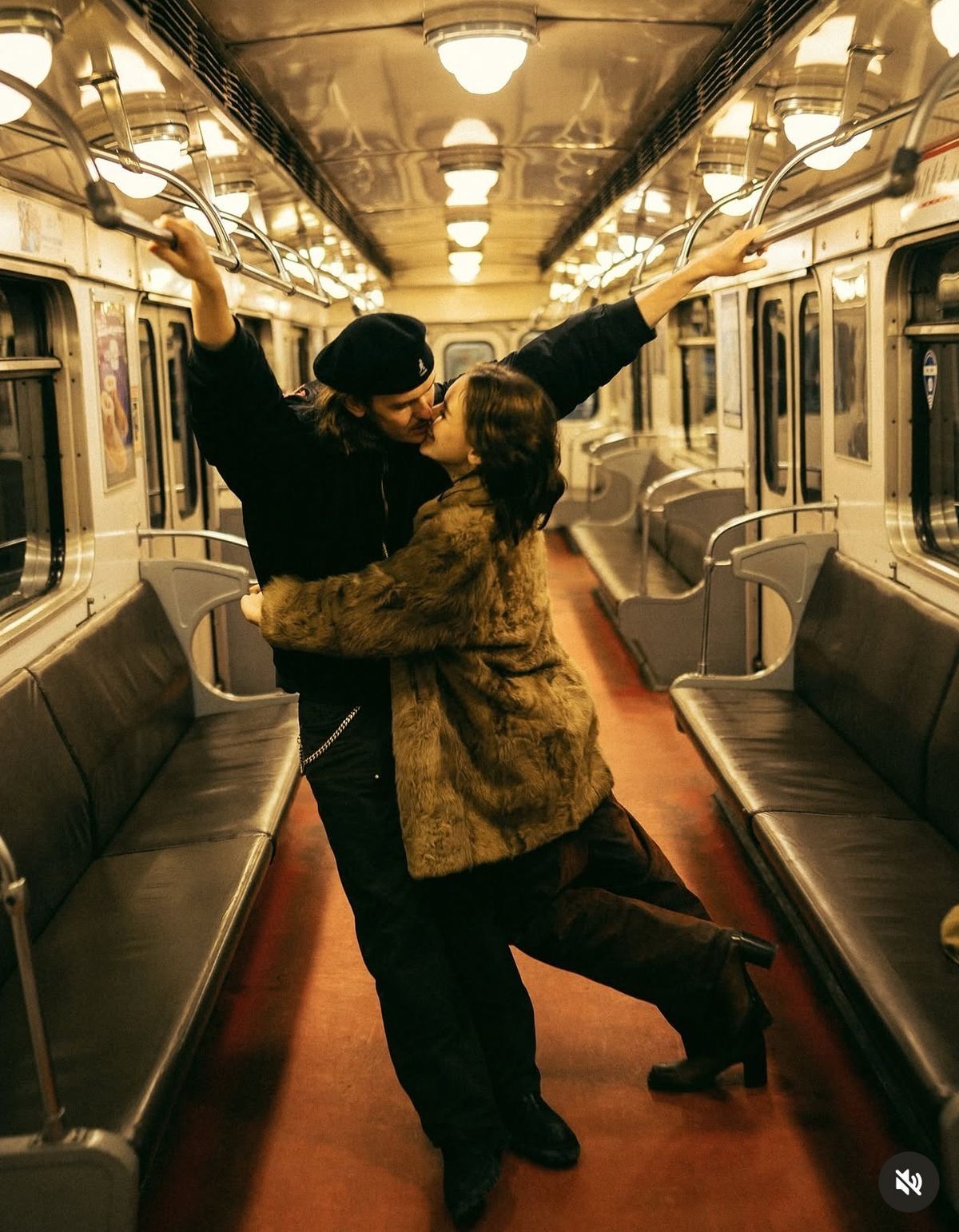 Couple sharing a romantic kiss and dance in an empty vintage subway car with warm golden lighting.