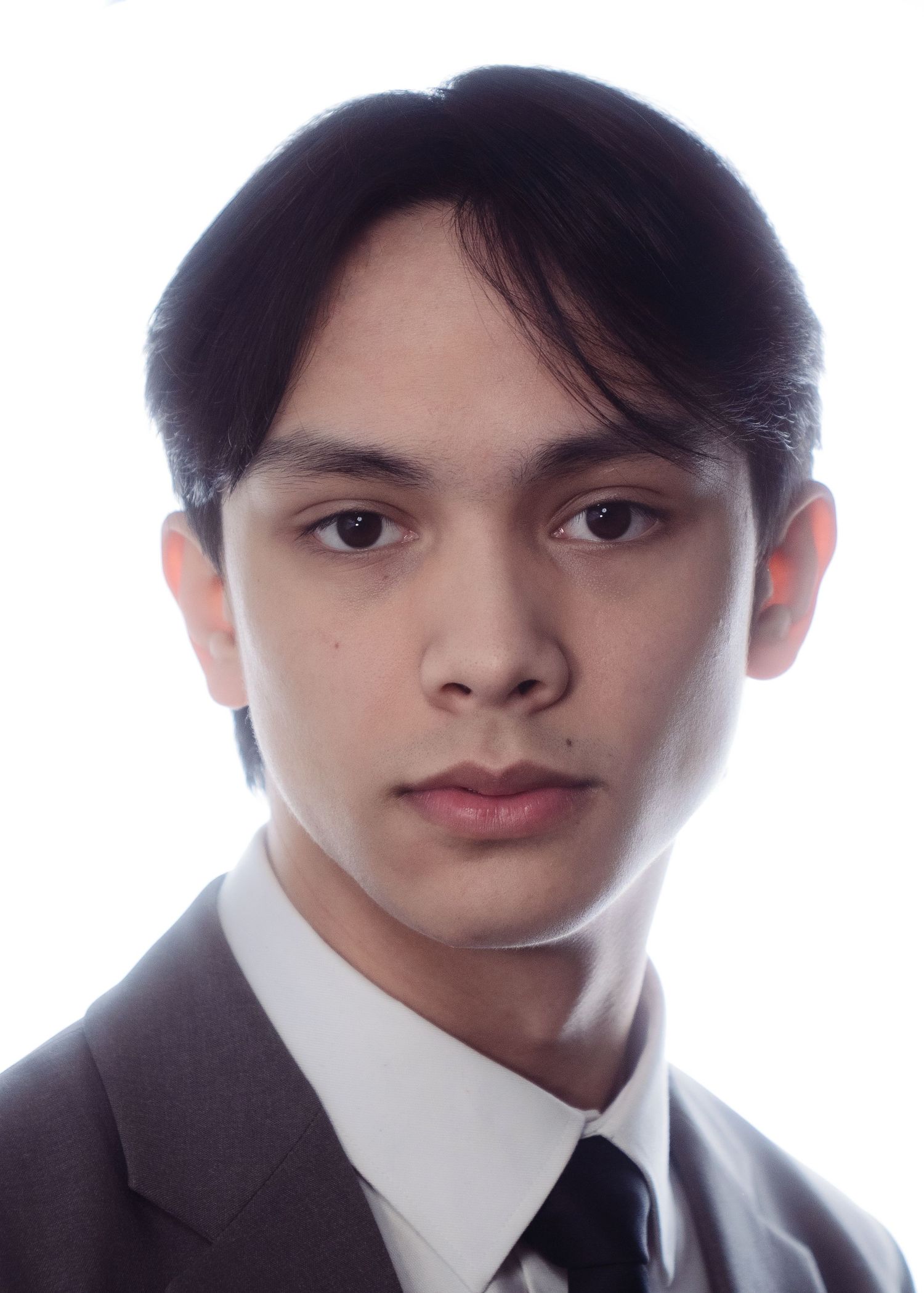 Young man with dark hair wearing a suit and tie, serious expression, professional headshot on white background.