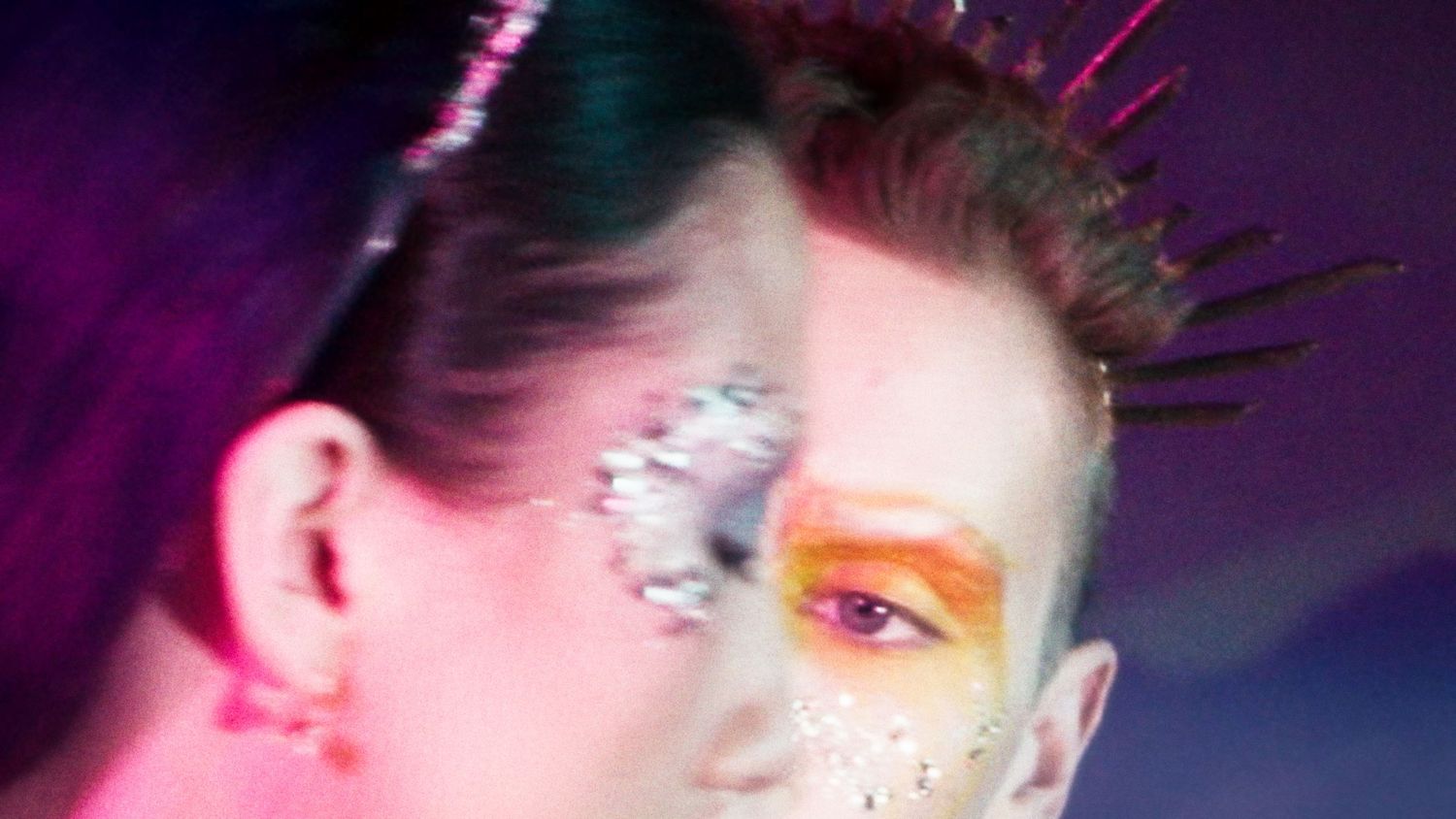 Two people with dramatic colorful glitter makeup and face paint at a party.