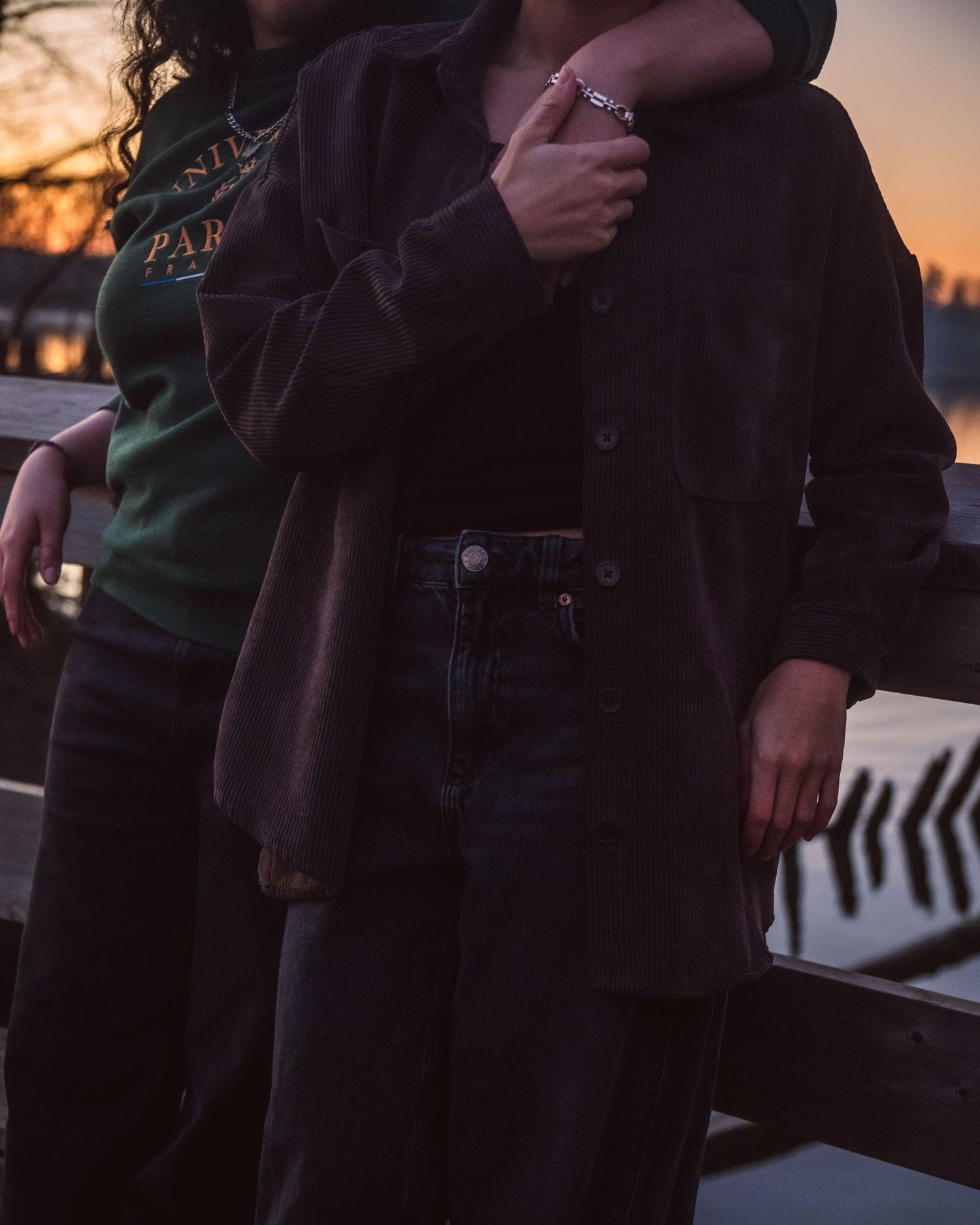Couple embracing at sunset on a bridge, woman in dark jacket and jeans holding partner in warm evening light.