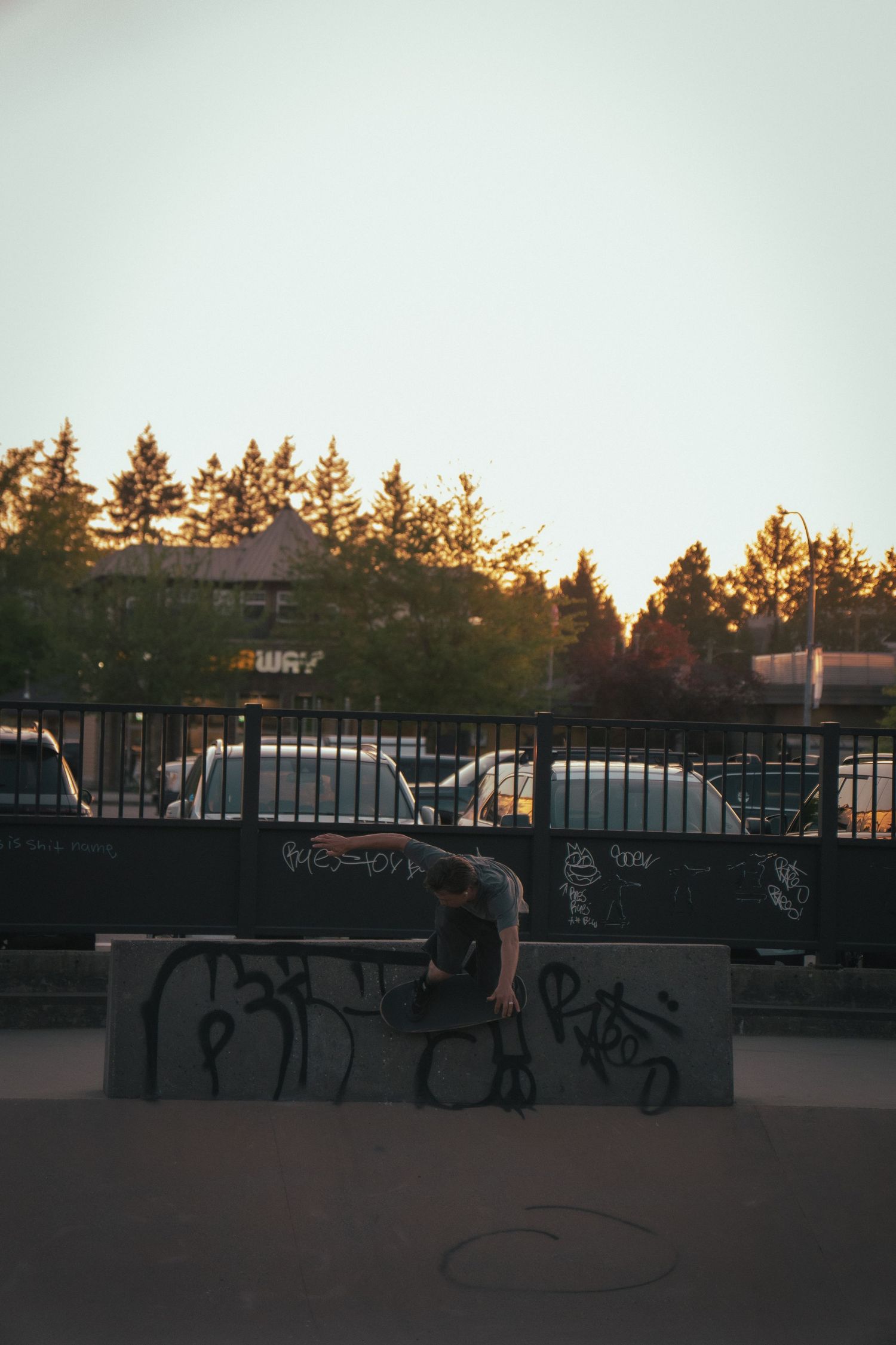 Skateboarder performing a trick on a graffiti-covered concrete ledge at sunset in a skate park.