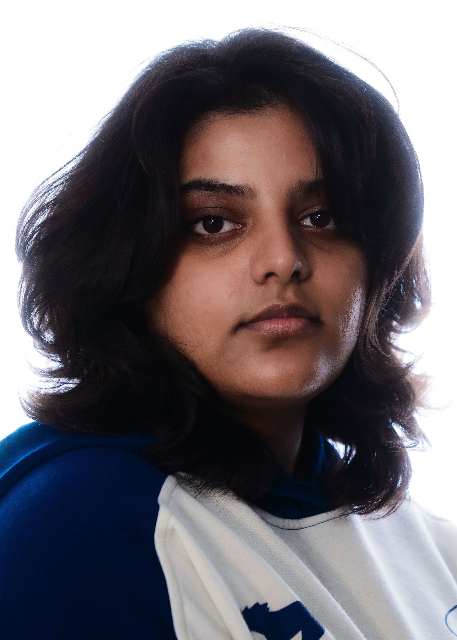 Young woman with dark wavy hair in a blue and white sports jersey, professional headshot on white background.