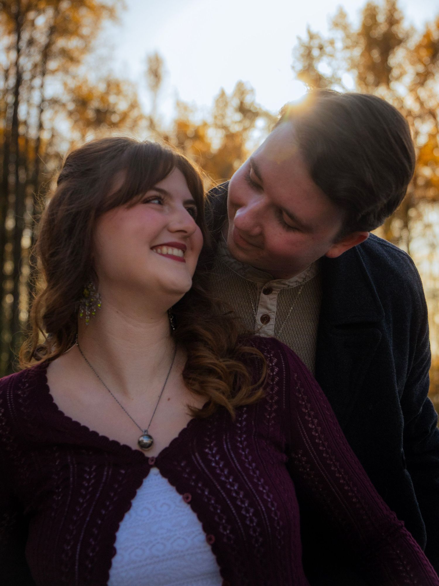 Young couple sharing a tender moment in golden sunset light surrounded by autumn trees, woman smiling warmly.